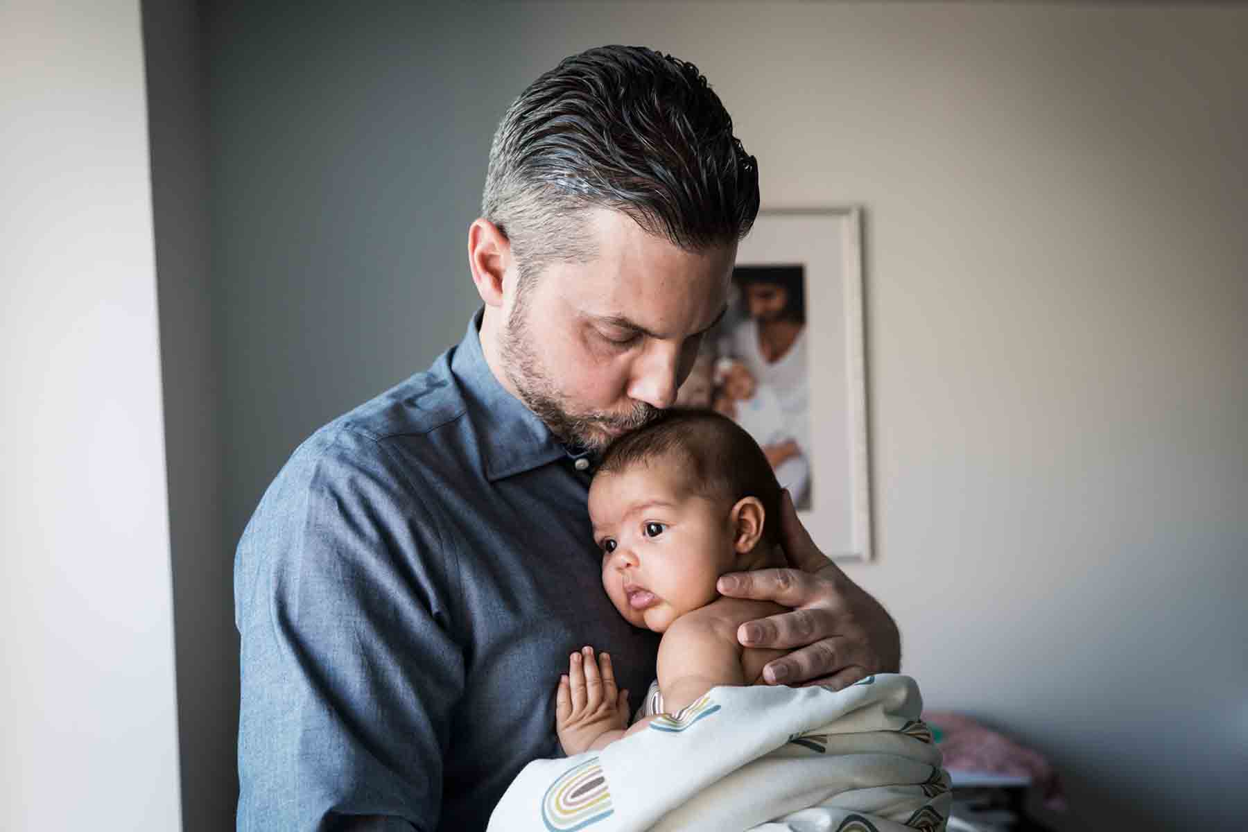 Father kissing newborn baby on the head in room with frame in background for an article on daddy and me photo shoot ideas