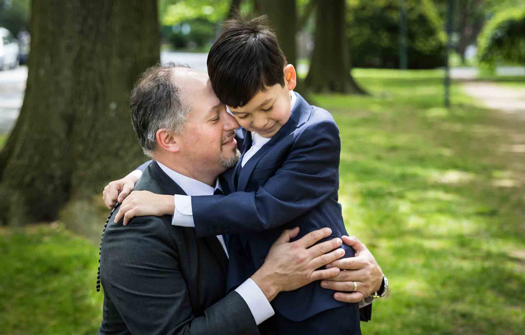 Father hugging son with both wearing suits in park for an article on daddy and me photo shoot ideas