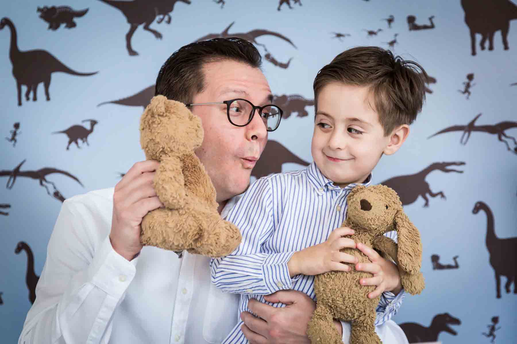 Father wearing glasses playing with little boy holding two stuffed animals for an article on daddy and me photo shoot ideas