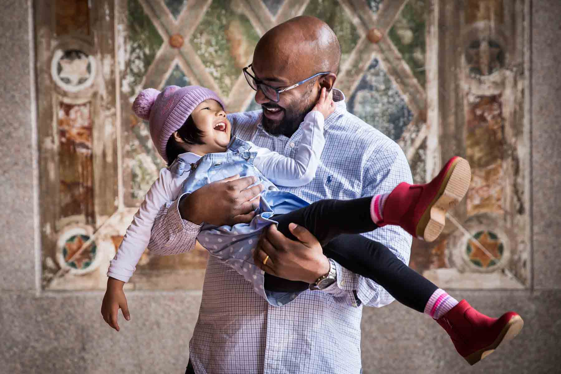 Man holding little girl wearing pink cap and red boots and laughing for an article on daddy and me photo shoot ideas