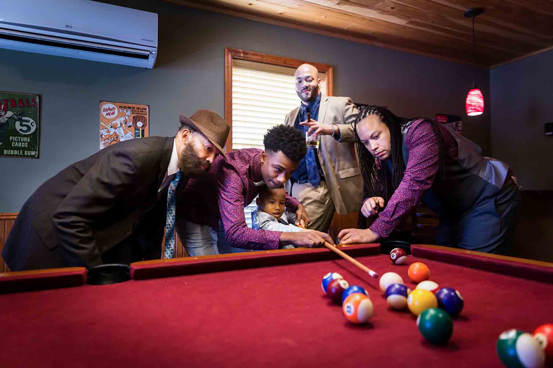 Four African American men showing little boy how to play pool for an article on daddy and me photo shoot ideas