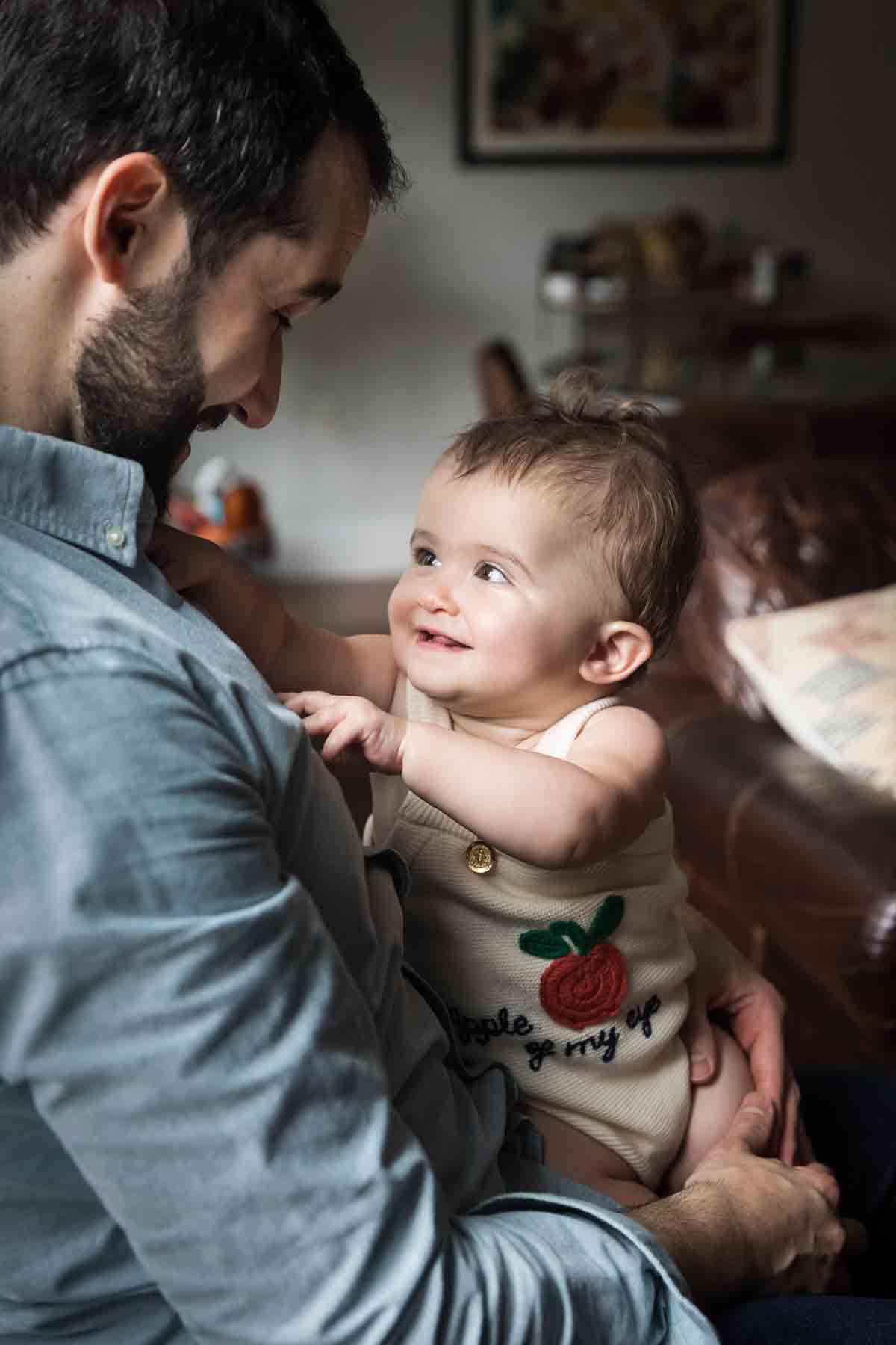 Toddler girl playing looking up at her father while playing in his lap for an article on daddy and me photo shoot ideas