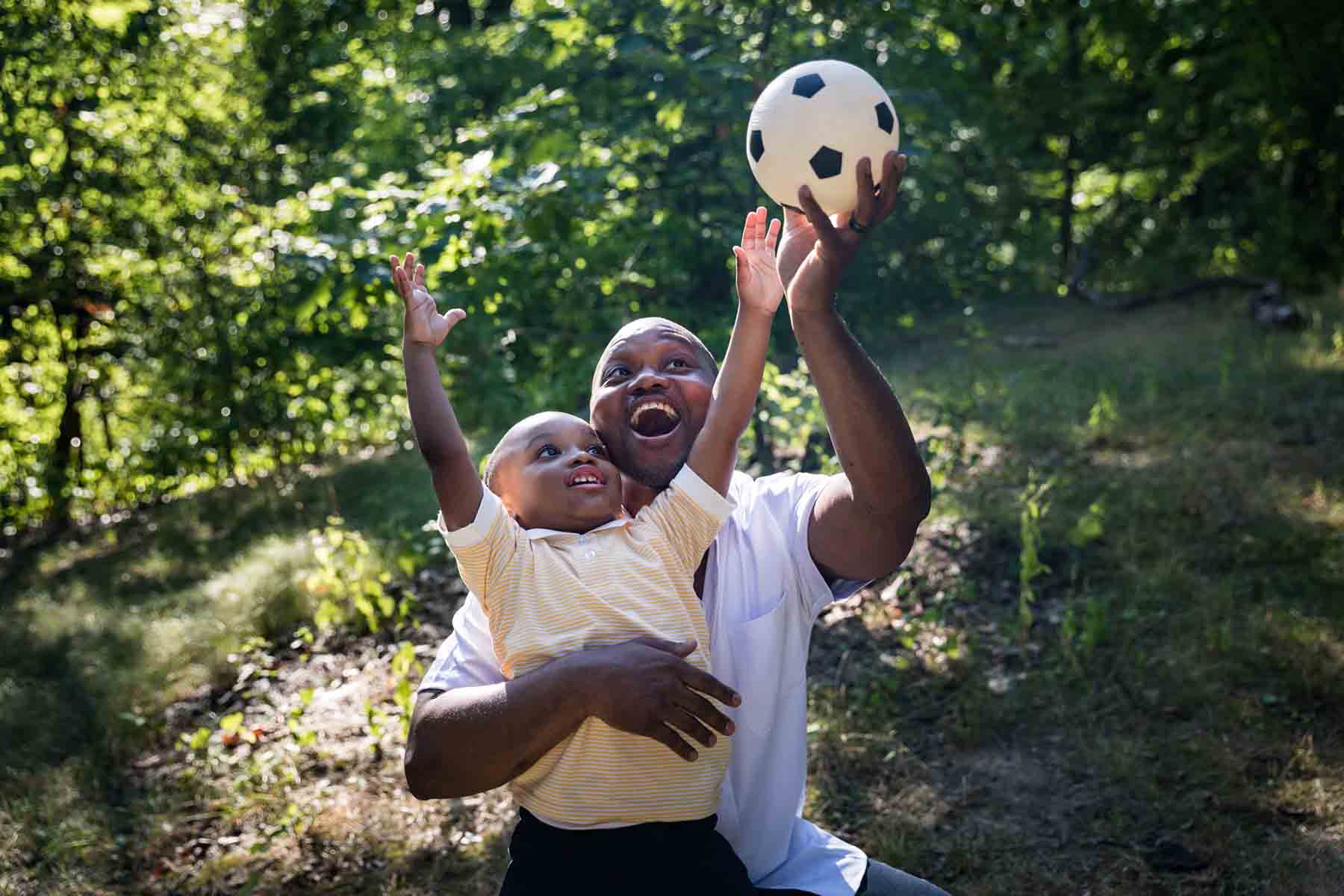 African American father and son playing with a soccer ball in a park for an article on daddy and me photo shoot ideas