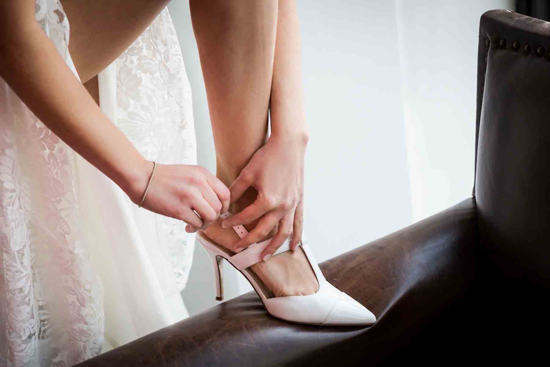 Close up of bride adjusting strap on white heel for an article on how to save money on wedding photography