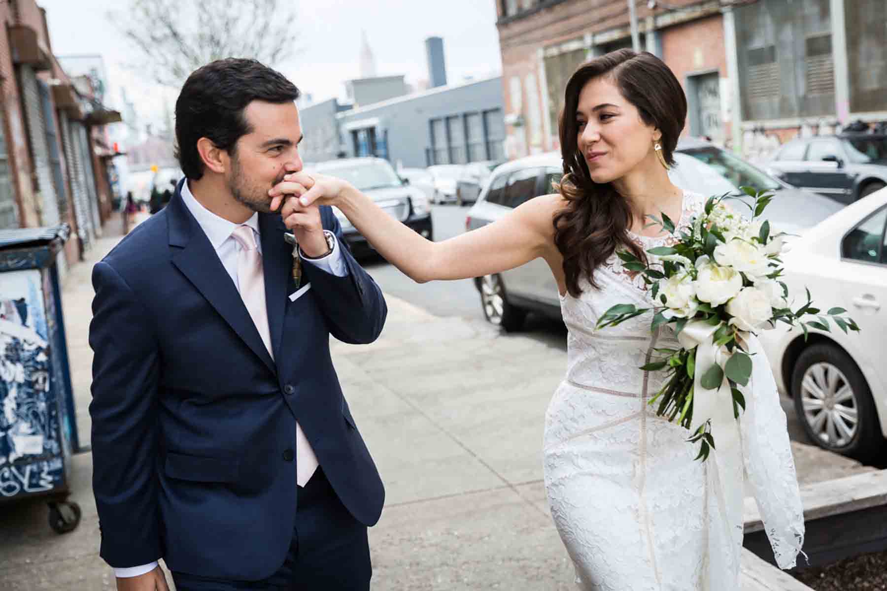 Groom kissing bride's hand on sidewalk for an article on how to save money on wedding photography