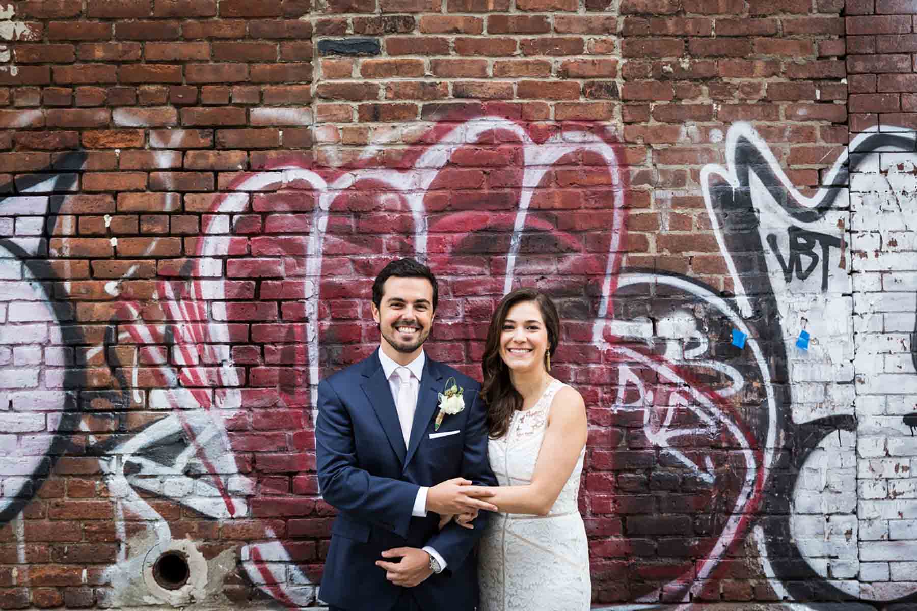 Bride and groom holding arms in front of graffiti brick wall for an article on how to save money on wedding photography