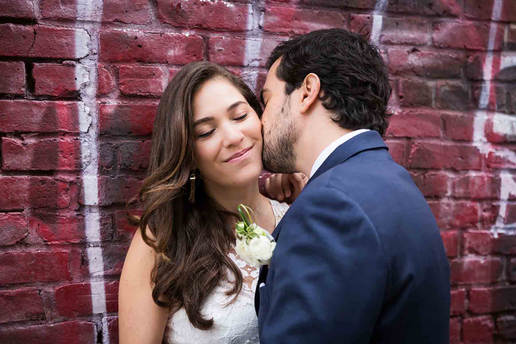 Groom kissing bride on the cheek in front of graffiti wall for an article on how to save money on wedding photography