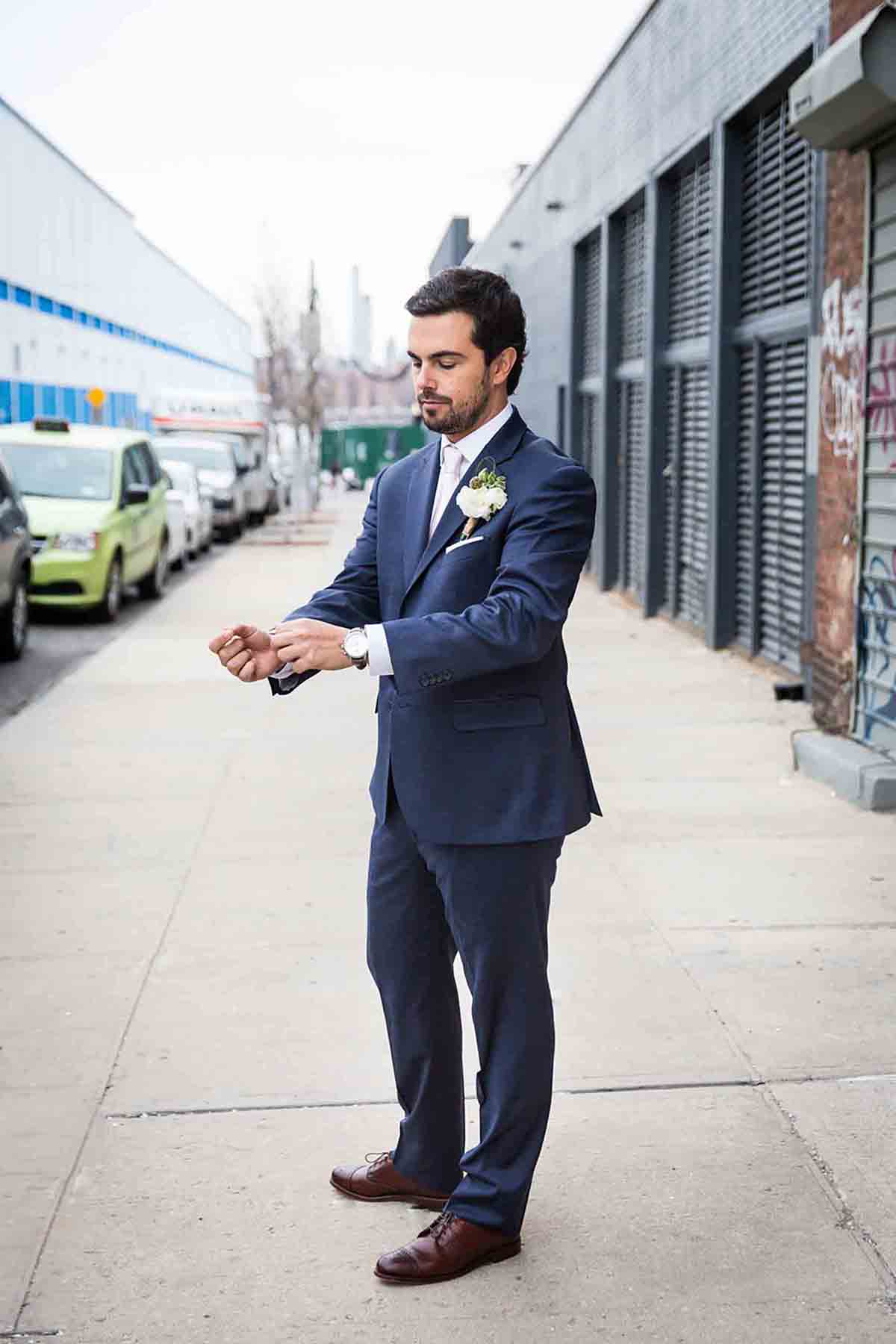 Groom wearing grey suit adjusting sleeve on sidewalk for an article on how to save money on wedding photography