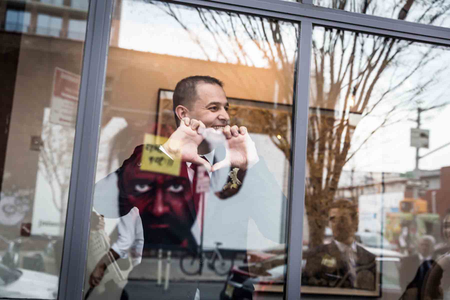 Man making heart sign with fingers through window for an article on how to save money on wedding photography