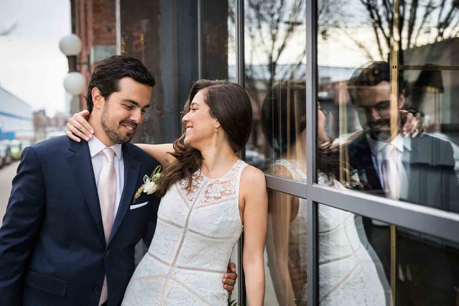 Bride and groom leaning against window for an article on how to save money on wedding photography