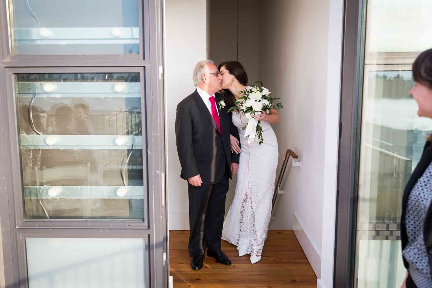 Bride kissing father on the cheek in hallway for an article on how to save money on wedding photography
