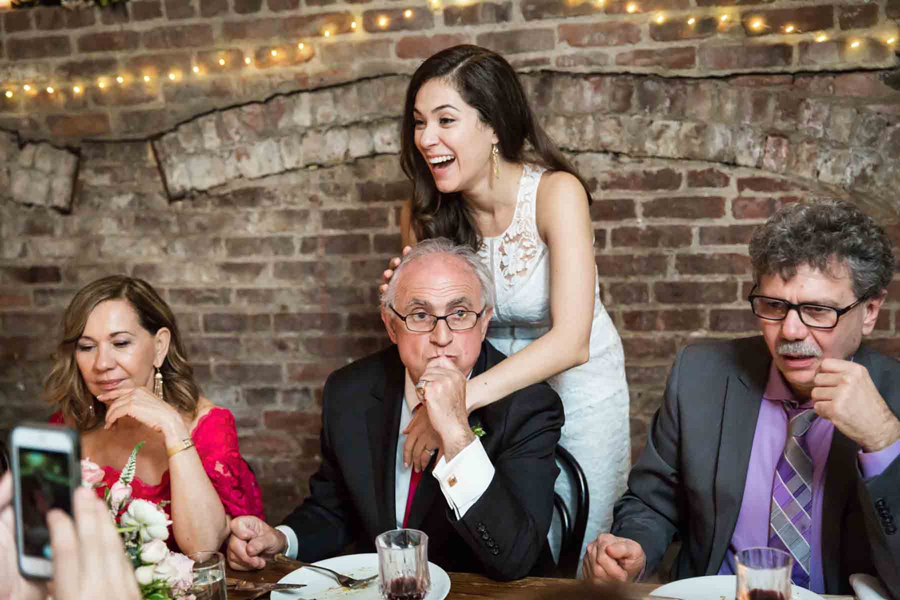 Bride hugging father's head in front of brick wall for an article on how to save money on wedding photography
