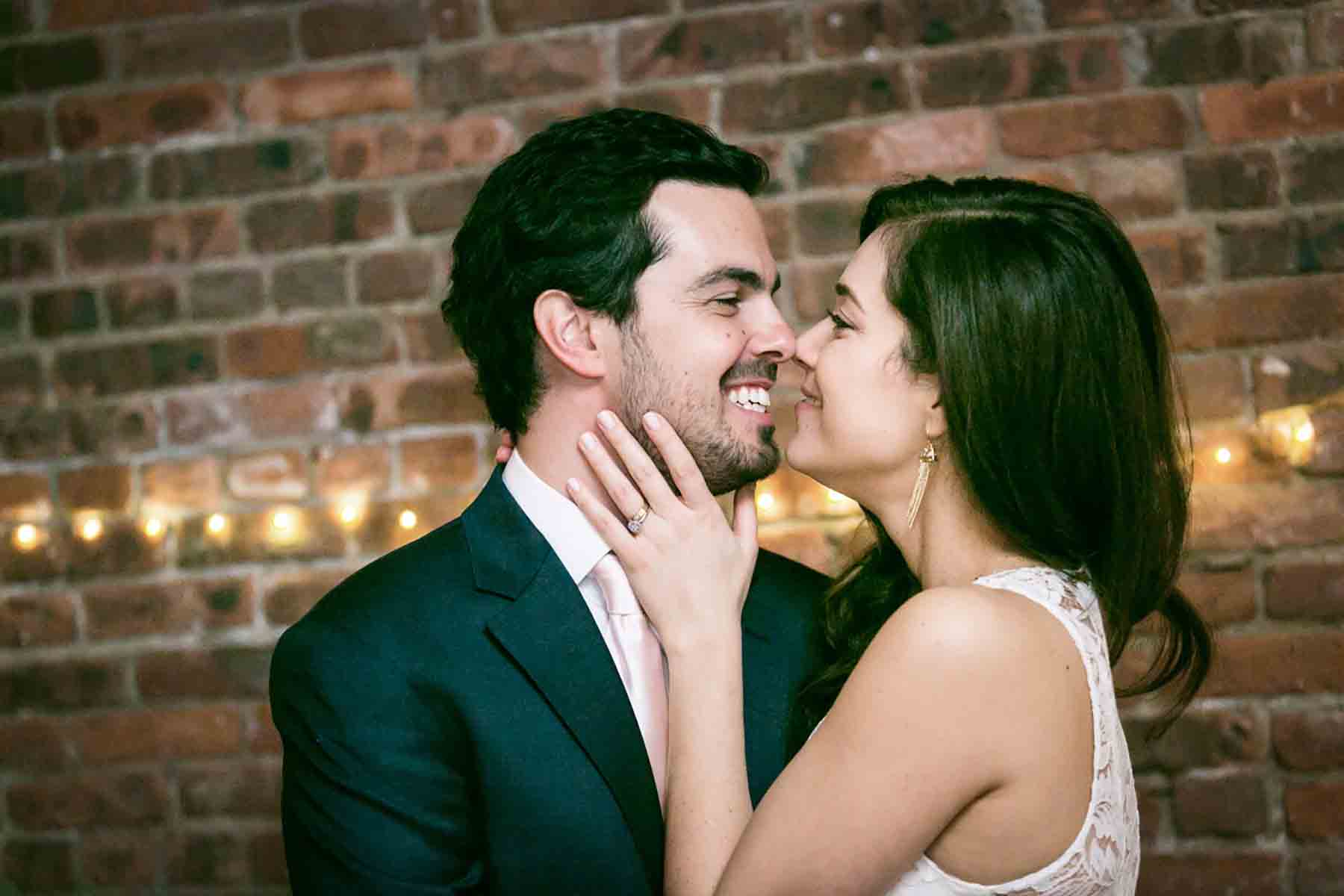 Bride holding groom's face in front of brick wall for an article on how to save money on wedding photography