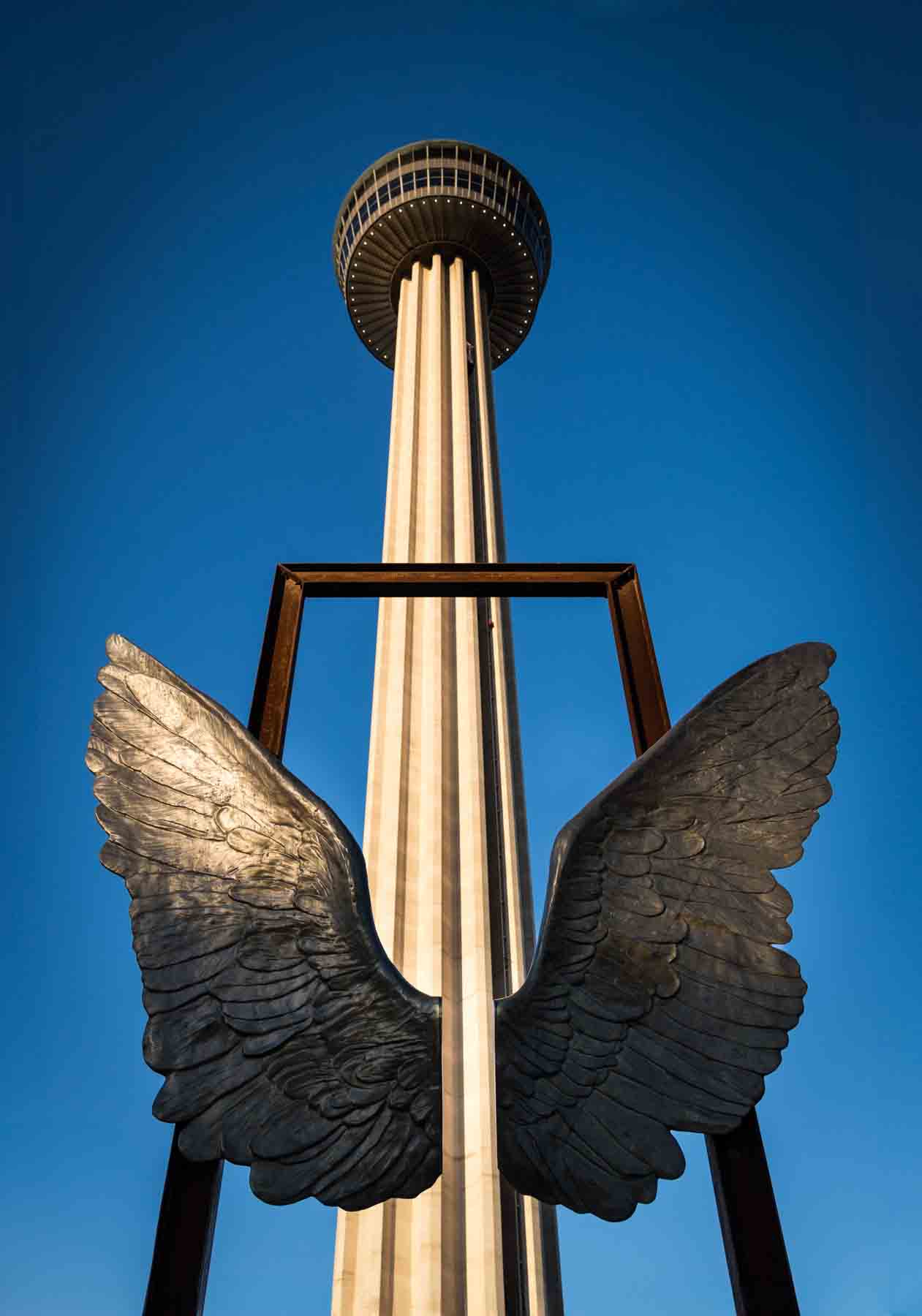 Wing sculpture in front of Tower of the Americas set against blue sky for an article on secret San Antonio photo shoot locations