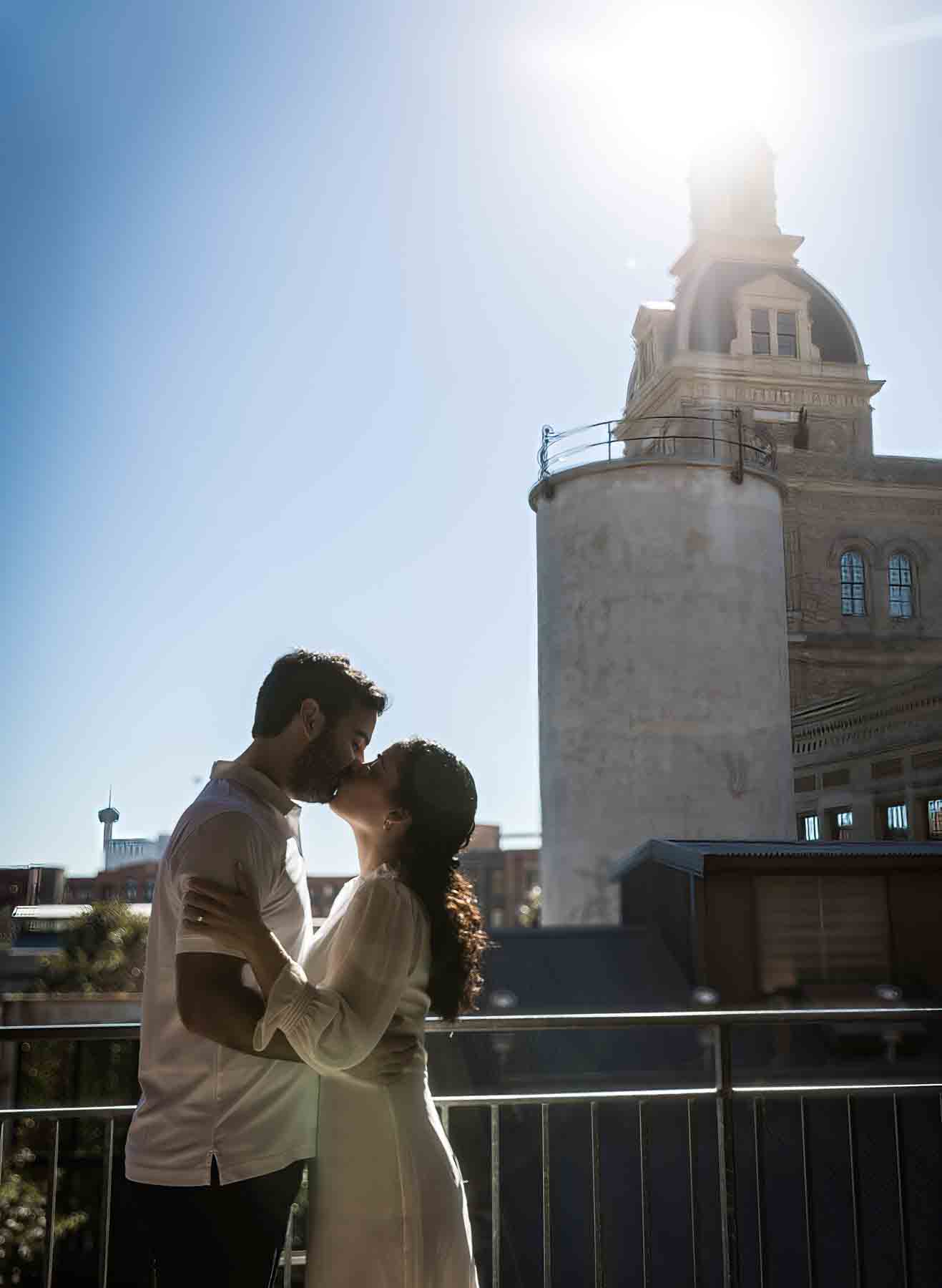 Couple kissing in front of sun with Emma Hotel in background for an article on secret San Antonio photo shoot locations