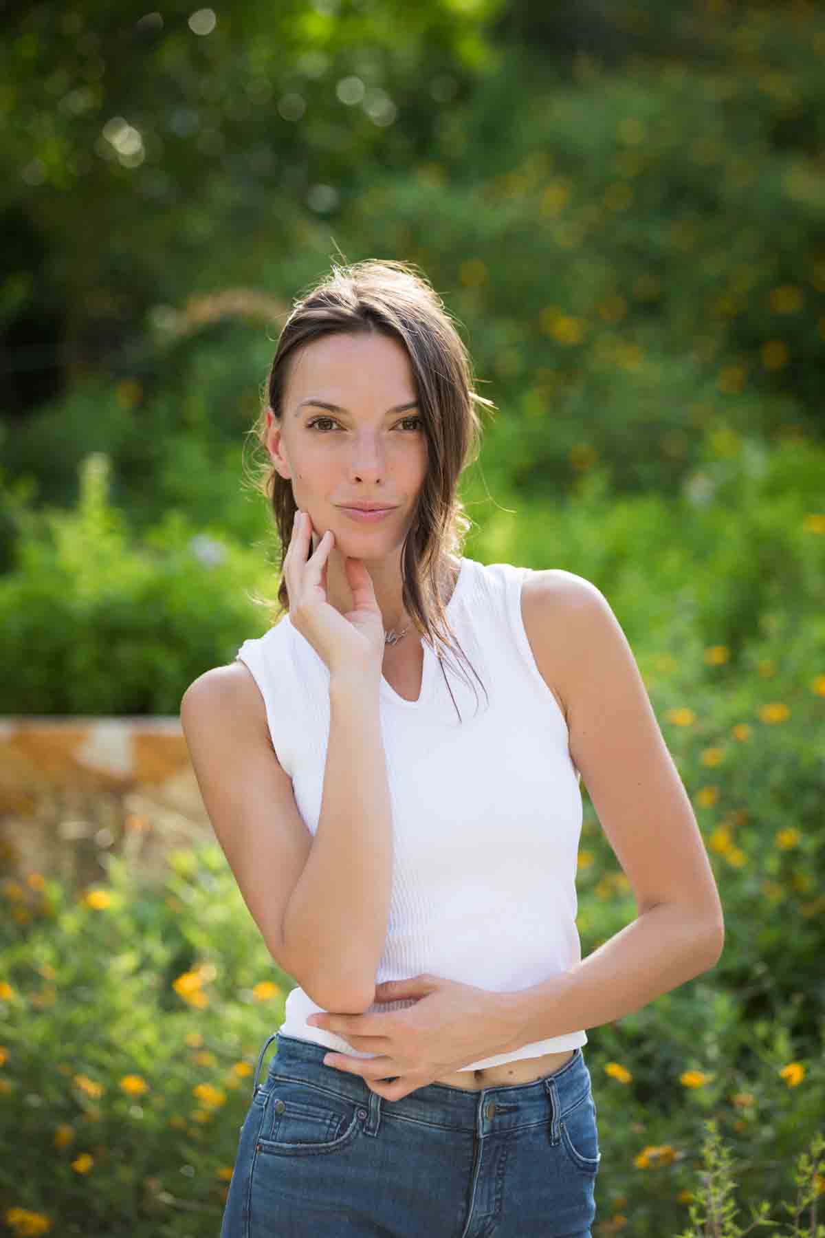 Model in white, sleeveless shirt posing in front of green bushes for an article announcing a downtown San Antonio photo shoot neighborhood discount