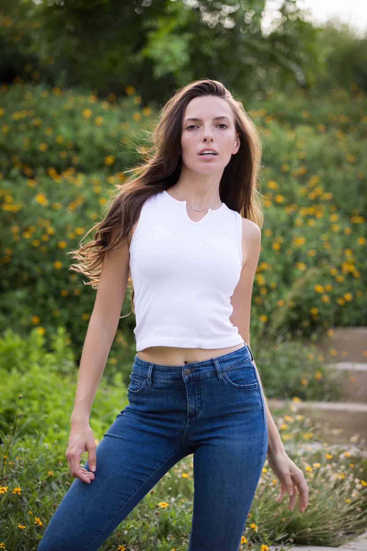 Model in white, sleeveless shirt posing in front of green bushes for an article announcing a downtown San Antonio photo shoot neighborhood discount