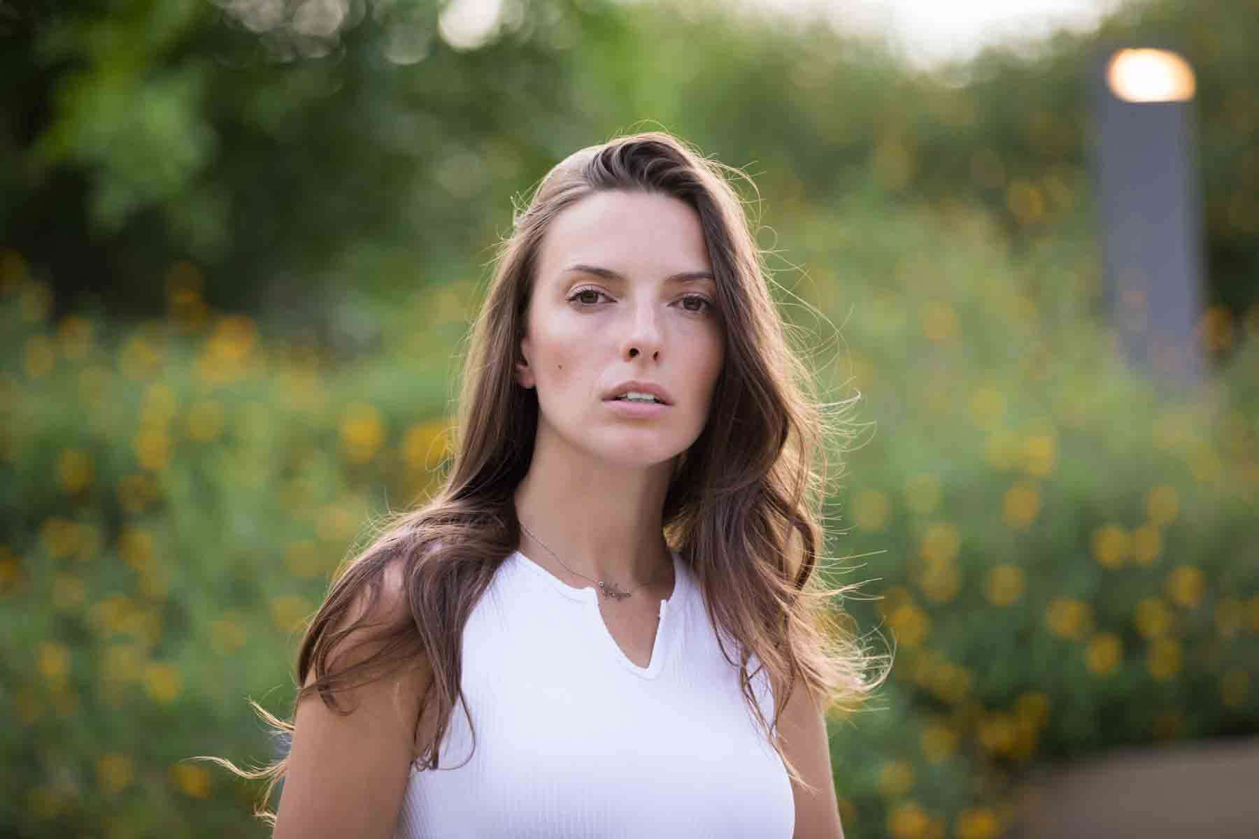 Model in white, sleeveless shirt posing in front of green bushes for an article announcing a downtown San Antonio photo shoot neighborhood discount