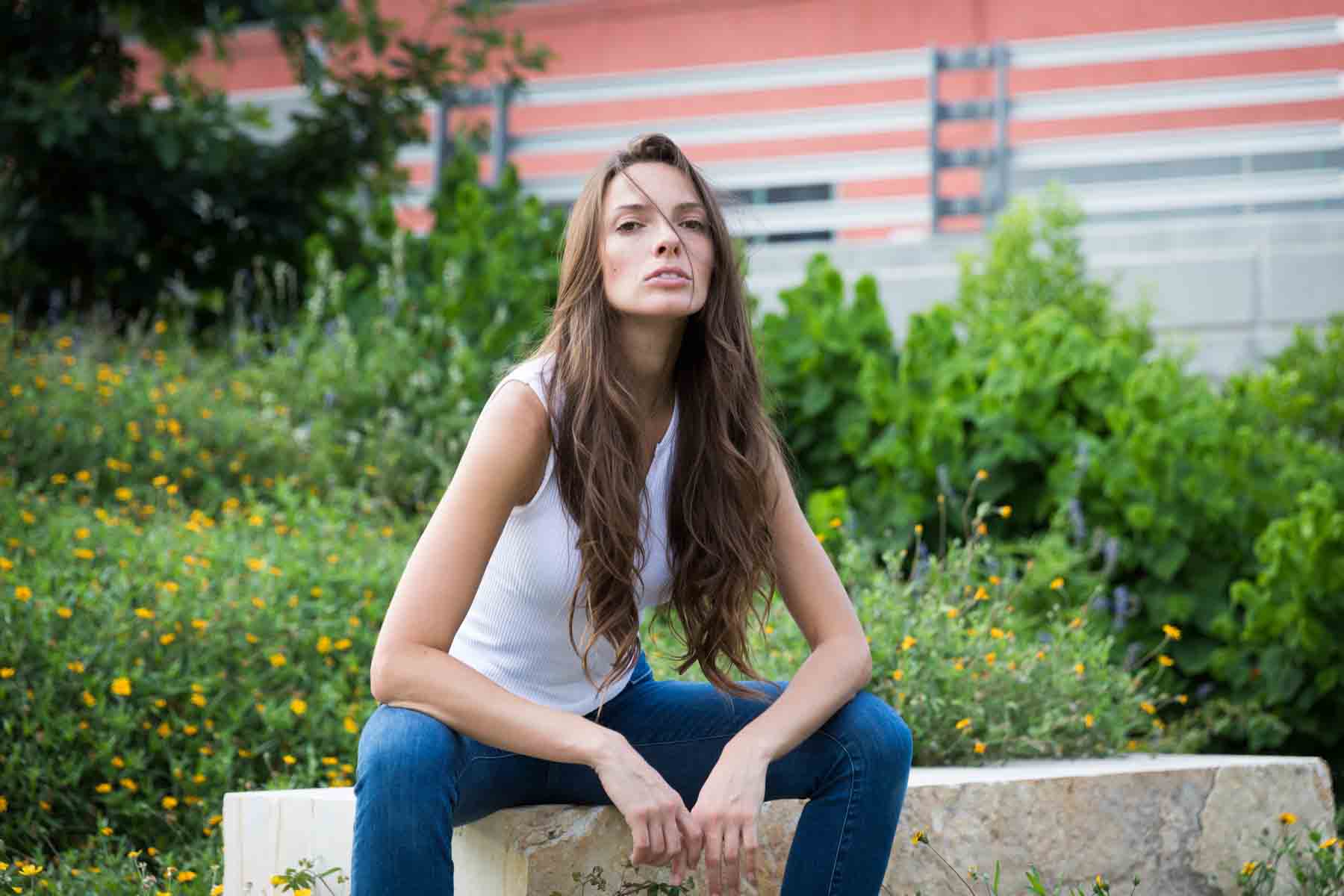 Model in white, sleeveless shirt posing in front of green bushes sitting on stone bench for an article announcing a downtown San Antonio photo shoot neighborhood discount