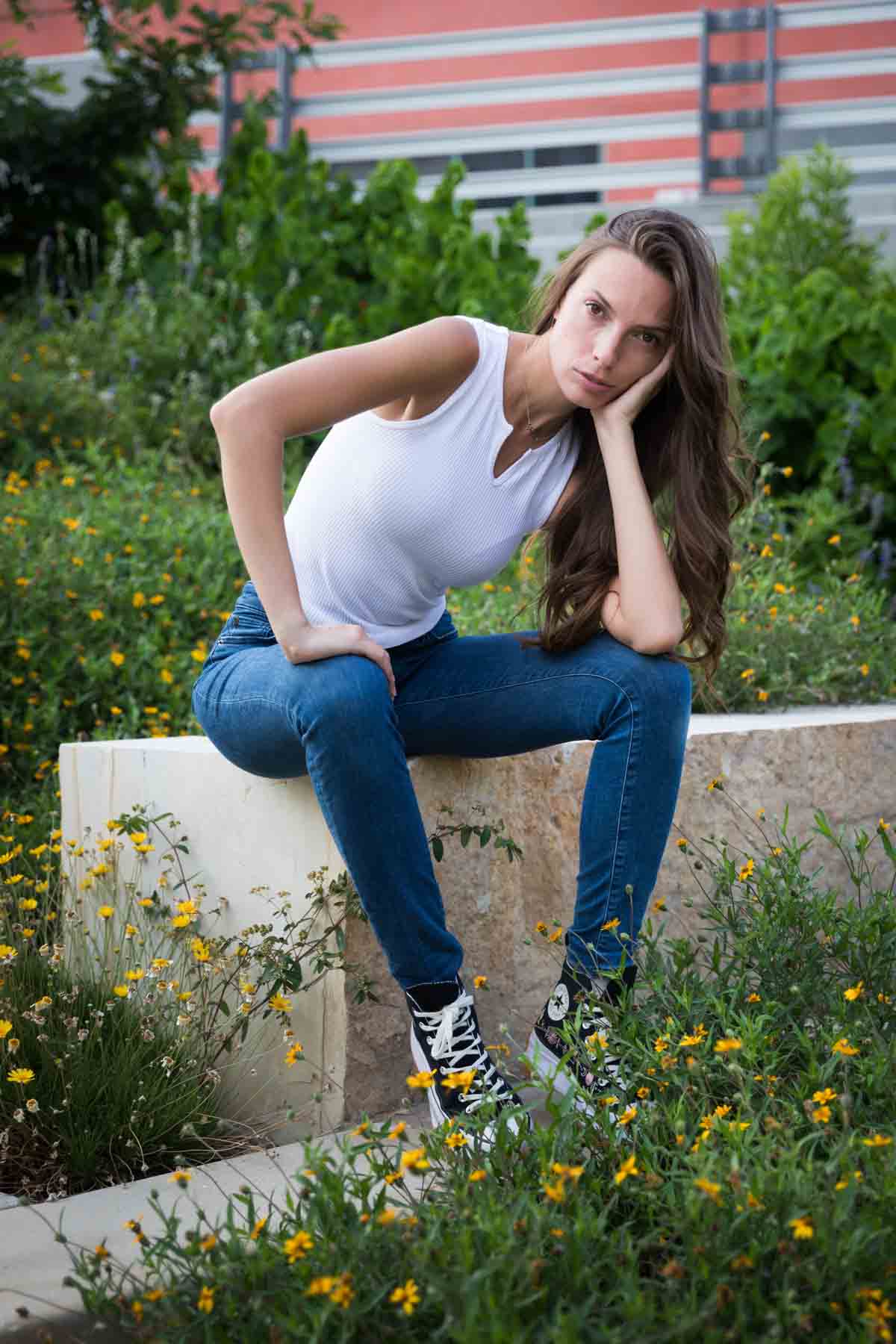 Model in white, sleeveless shirt posing in front of green bushes sitting on stone bench for an article announcing a downtown San Antonio photo shoot neighborhood discount