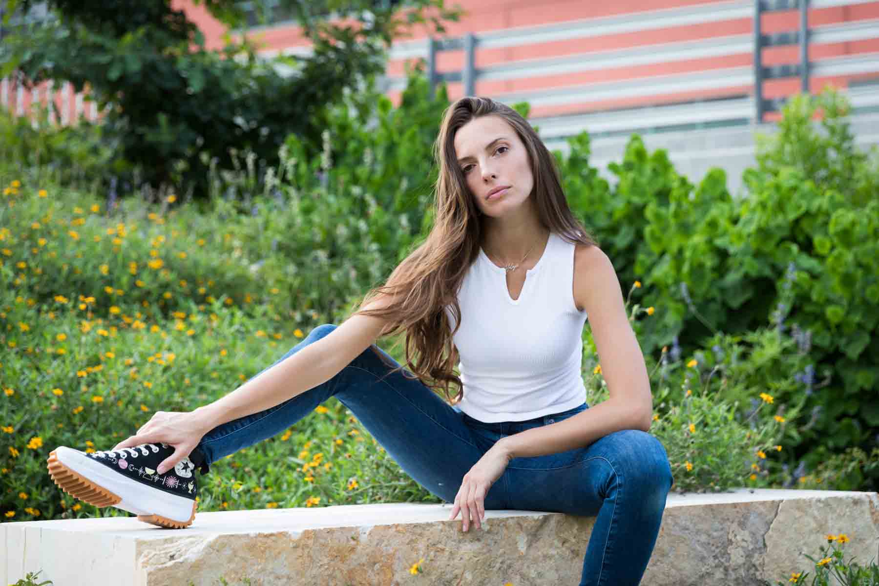 Model in white, sleeveless shirt posing in front of green bushes sitting on stone bench for an article announcing a downtown San Antonio photo shoot neighborhood discount