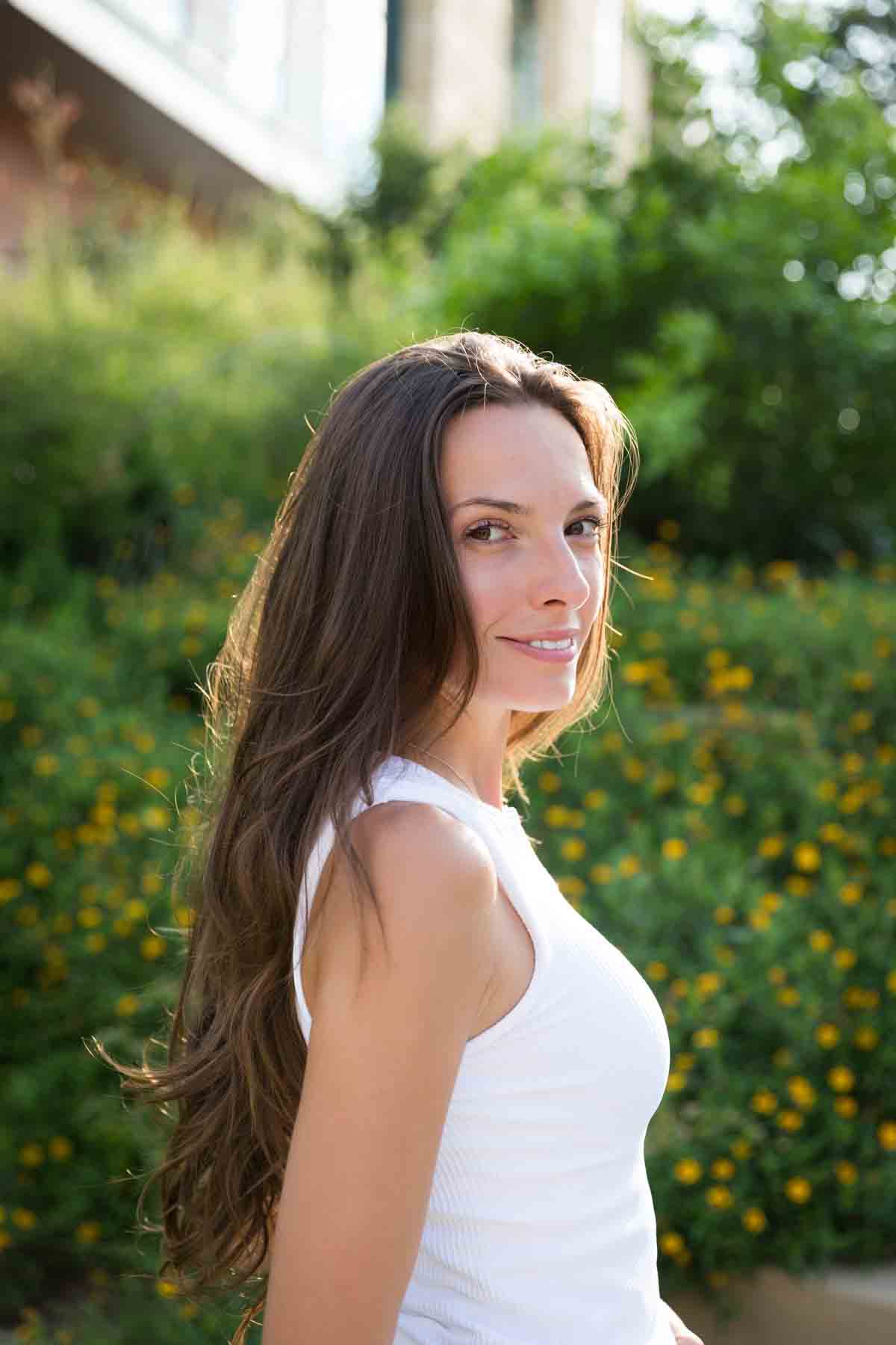 Model in white, sleeveless shirt posing in front of green bushes for an article announcing a downtown San Antonio photo shoot neighborhood discount