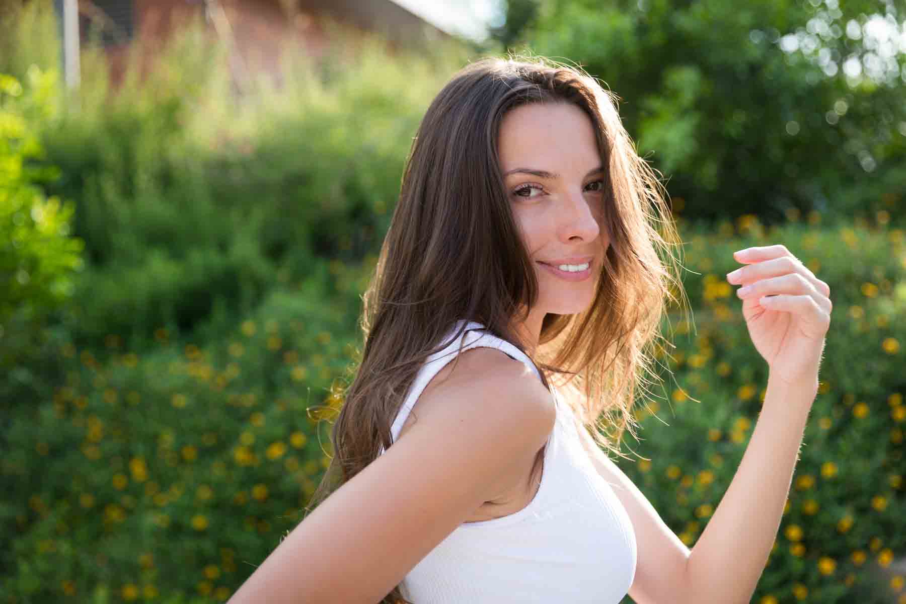 Model in white, sleeveless shirt posing in front of green bushes for an article announcing a downtown San Antonio photo shoot neighborhood discount