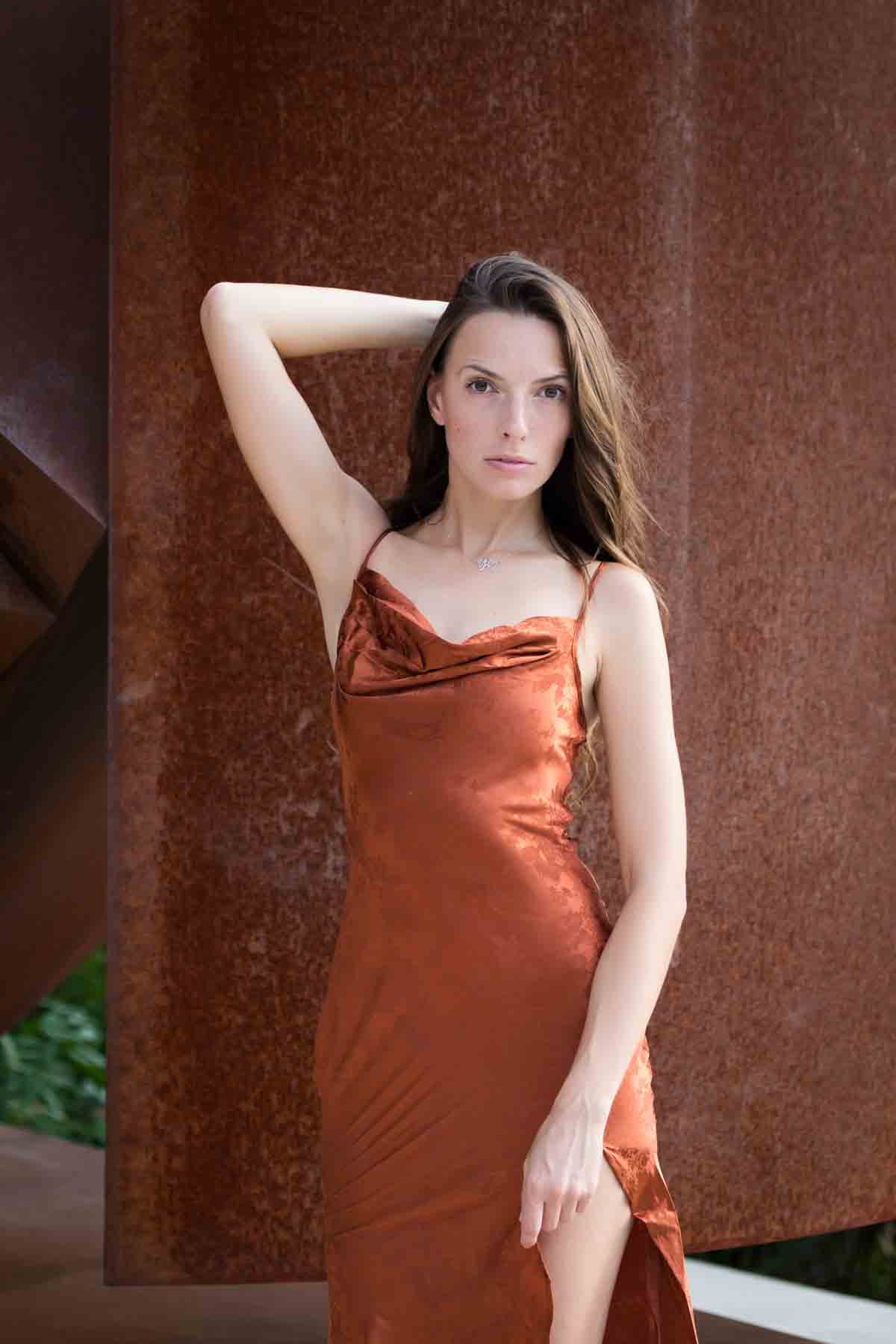 Model in rust-colored dress posing in front of rusted sculpture for an article announcing a downtown San Antonio photo shoot neighborhood discount