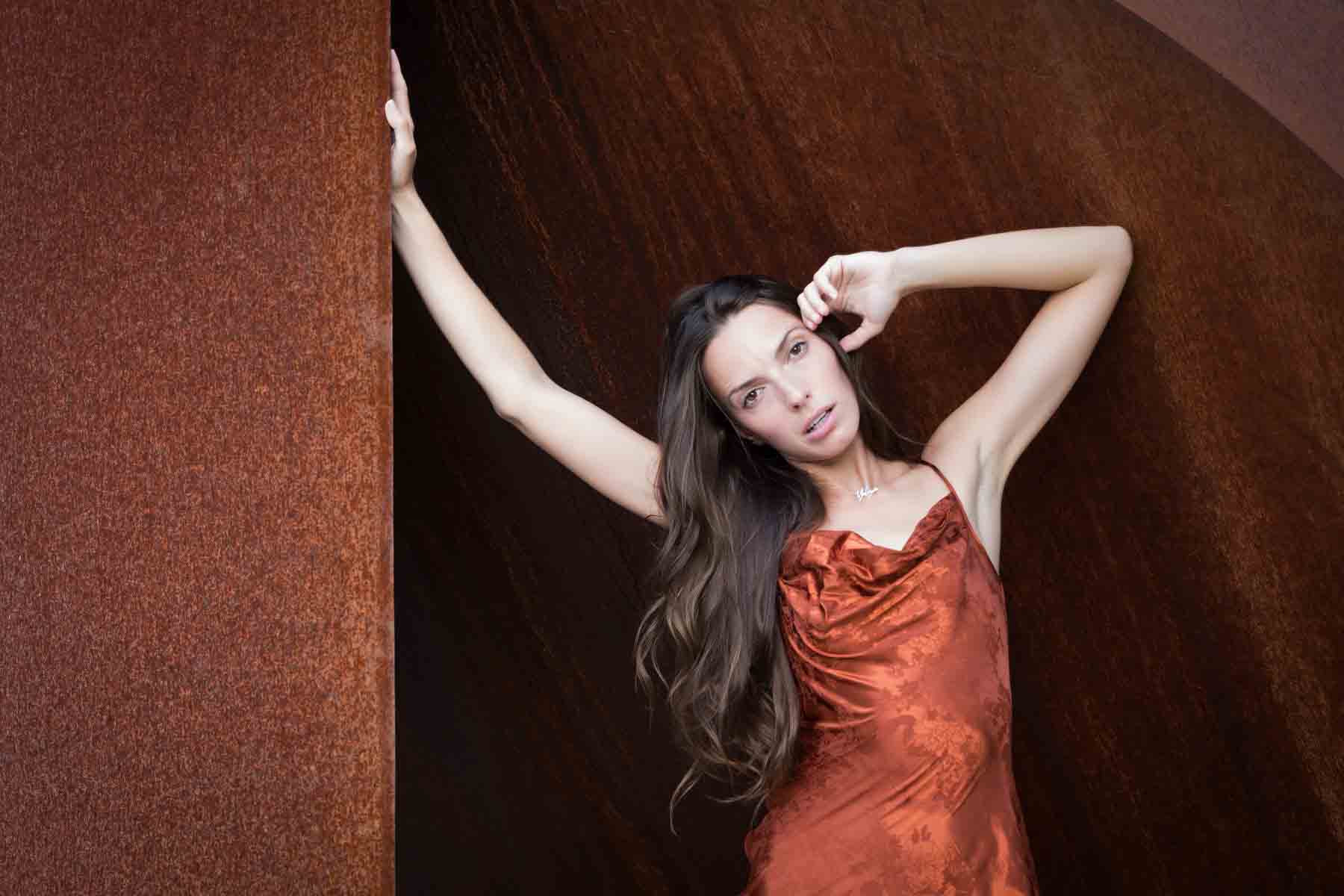 Model in rust-colored dress posing in front of rusted sculpture for an article announcing a downtown San Antonio photo shoot neighborhood discount