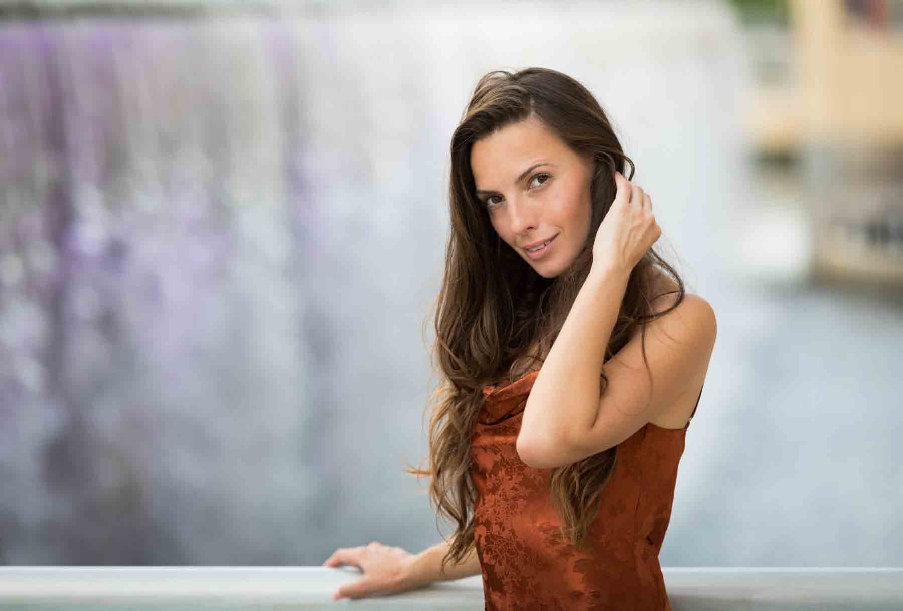 Model in rust-colored dress posing in front of waterfall for an article announcing a downtown San Antonio photo shoot neighborhood discount