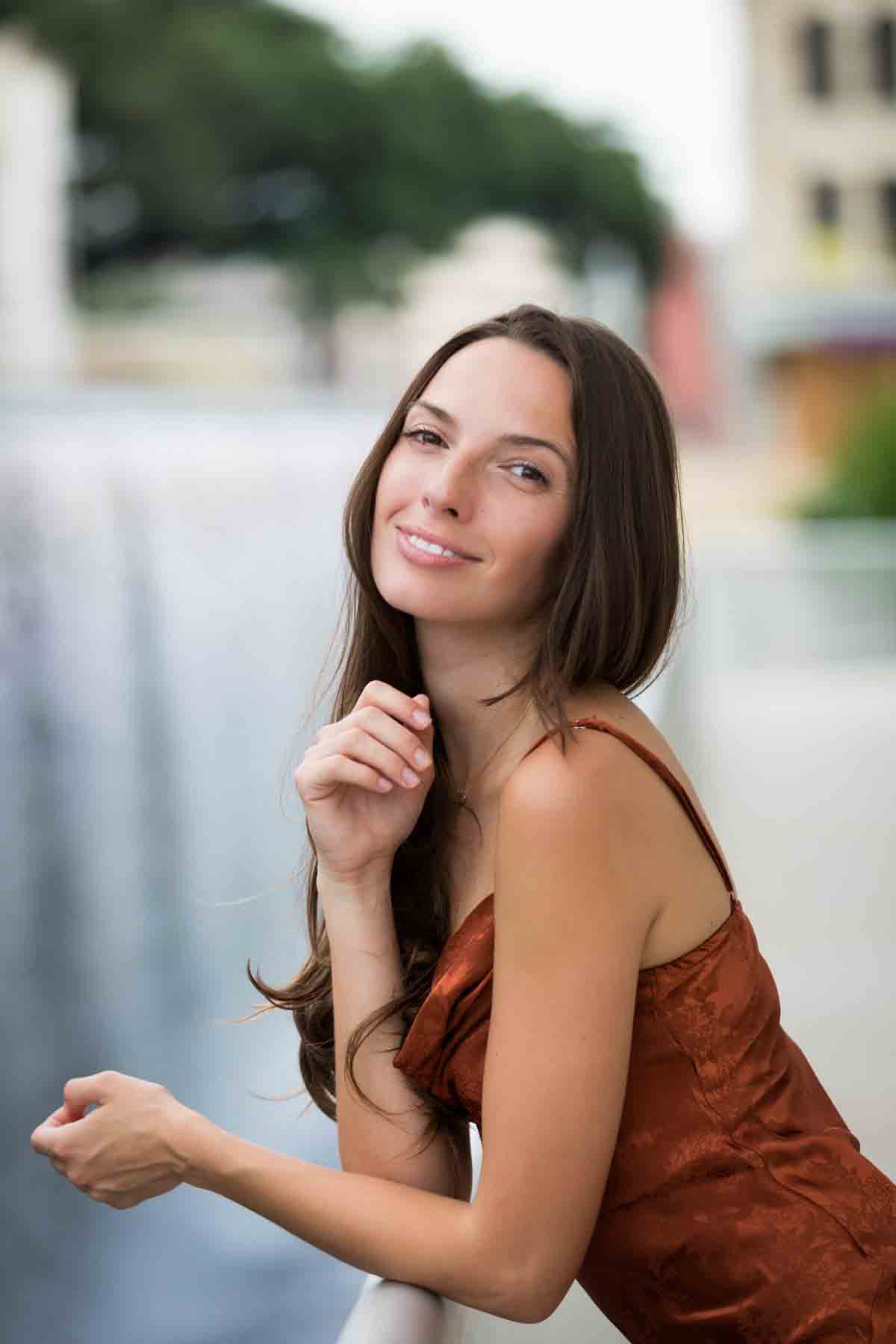 Model in rust-colored dress posing in front of waterfall for an article announcing a downtown San Antonio photo shoot neighborhood discount