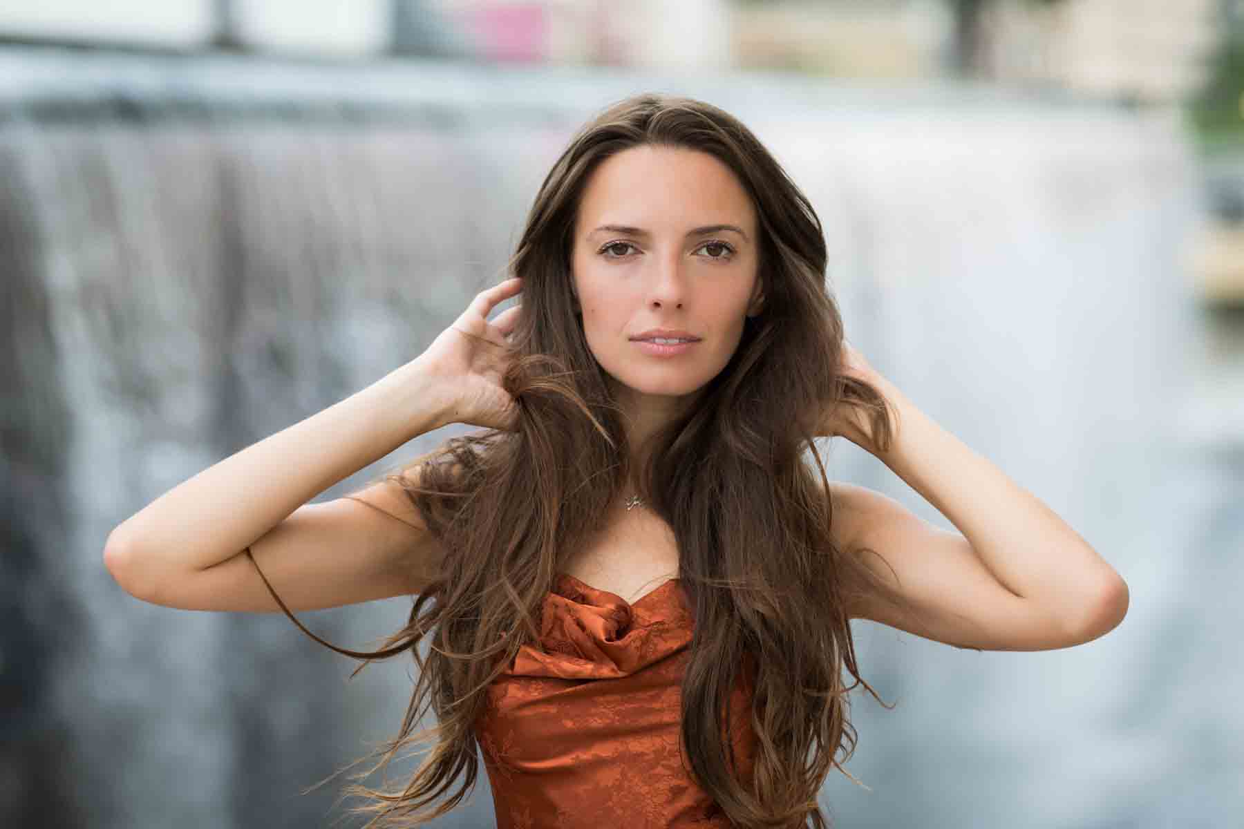 Model in rust-colored dress posing in front of waterfall for an article announcing a downtown San Antonio photo shoot neighborhood discount