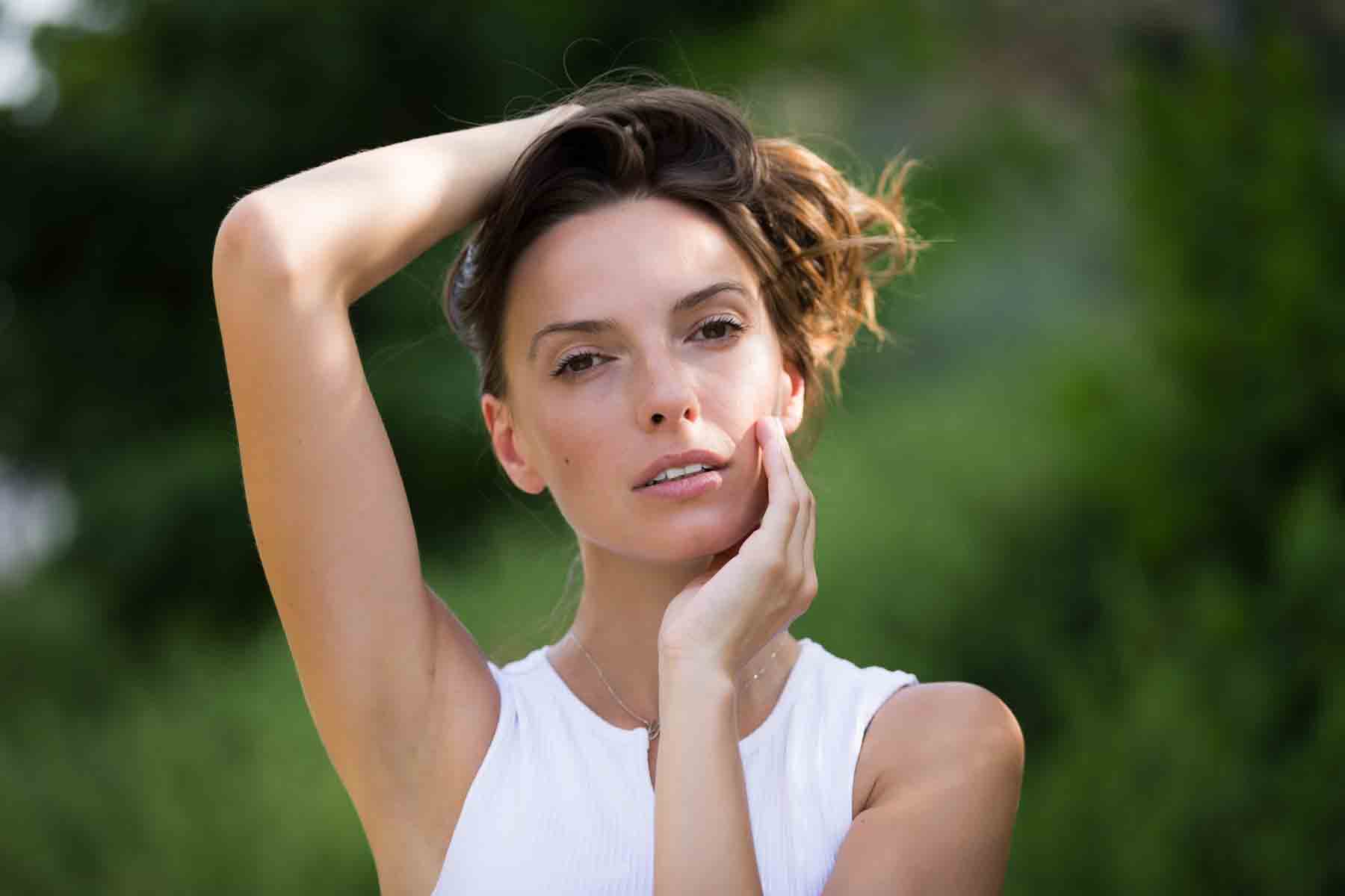 Model in white, sleeveless shirt posing in front of green bushes for an article announcing a downtown San Antonio photo shoot neighborhood discount