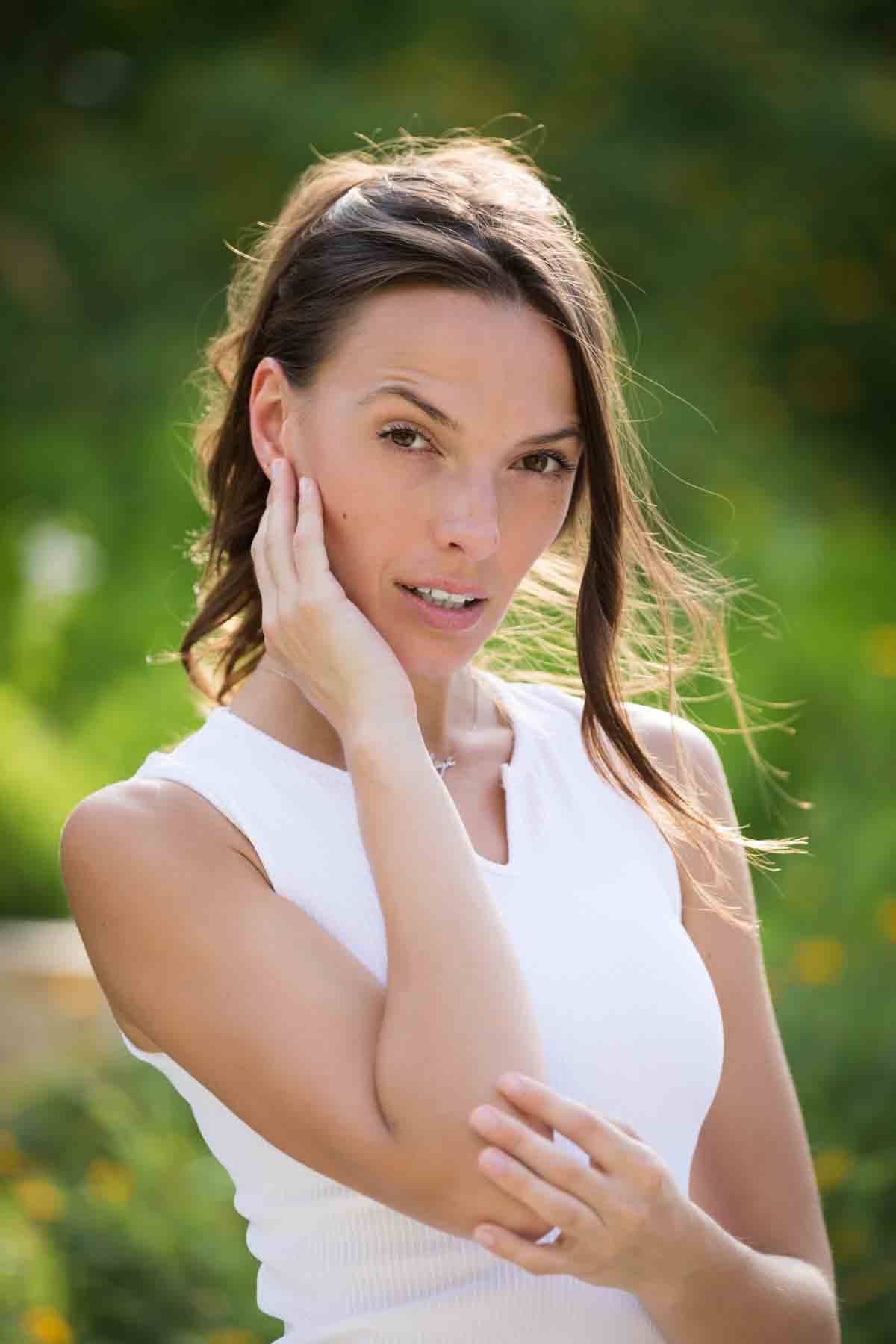 Model in white, sleeveless shirt posing in front of green bushes for an article announcing a downtown San Antonio photo shoot neighborhood discount