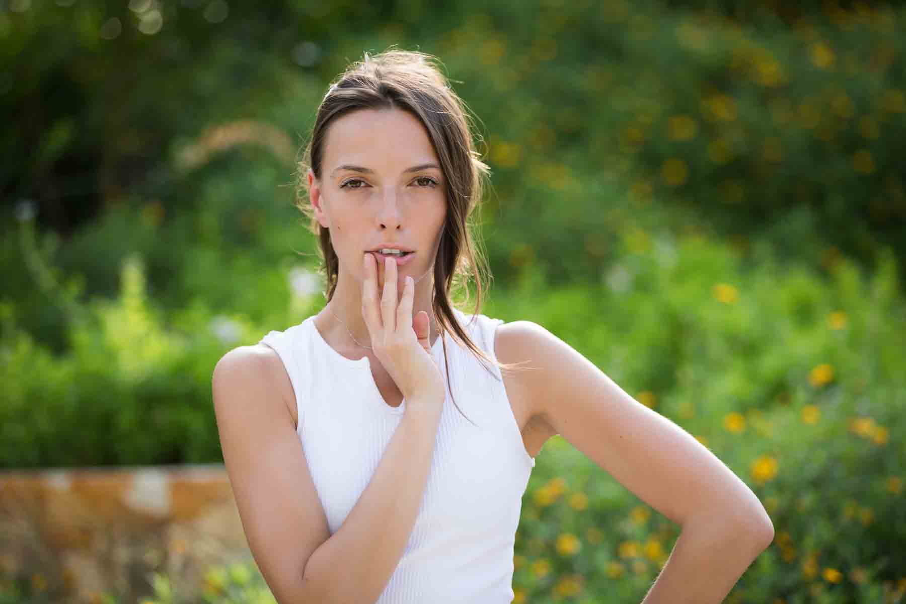 Model in white, sleeveless shirt posing in front of green bushes for an article announcing a downtown San Antonio photo shoot neighborhood discount