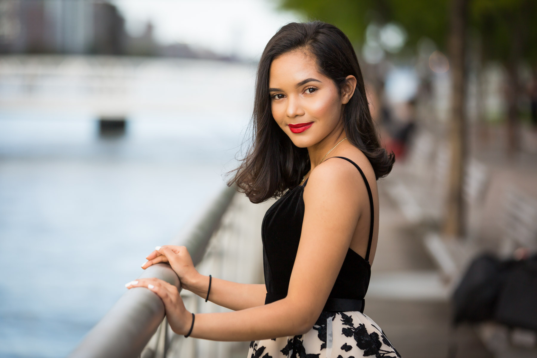 Smiling woman with brown hair and red lipstick holding onto railing for an article on how to beat the summer heat during a photo shoot