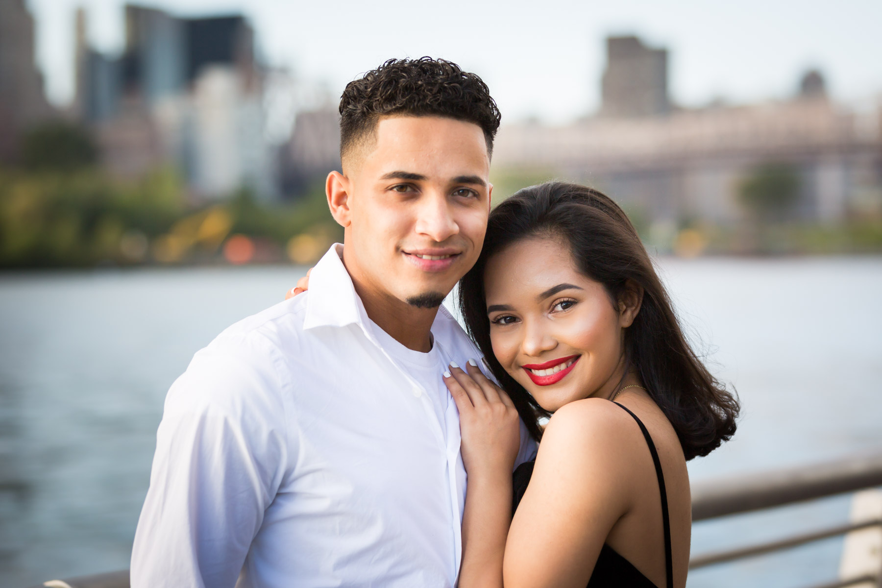 Couple looking into camera in front of railing with city skyline in background for an article on how to beat the summer heat during a photo shoot