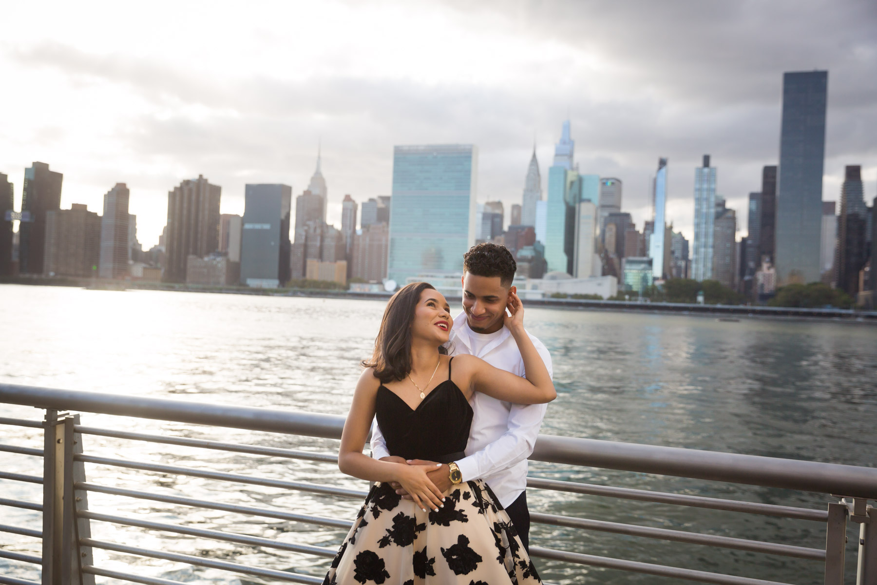 Couple hugging in front of railing with city skyline in background for an article on how to beat the summer heat during a photo shoot