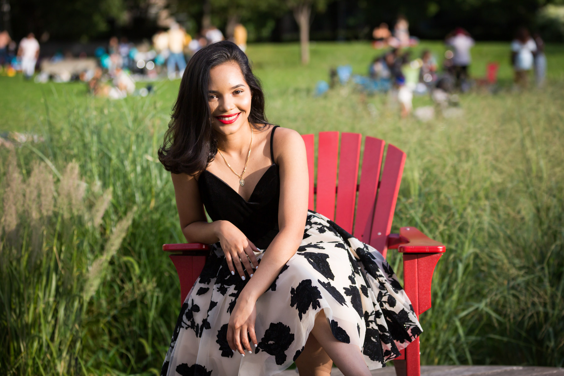 Smiling woman with brown hair and red lipstick sitting in red adirondack chair for an article on how to beat the summer heat during a photo shoot