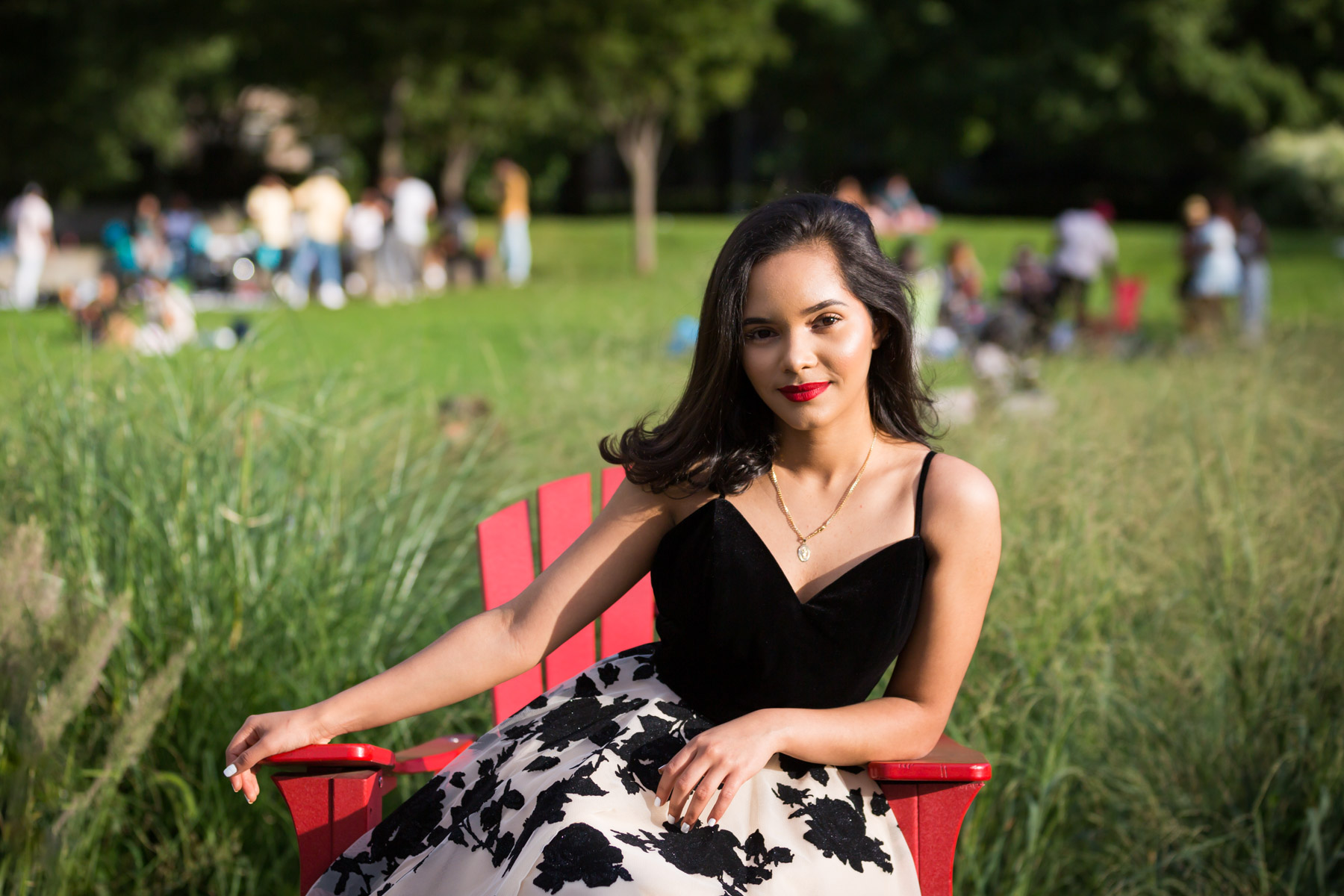 Smiling woman with brown hair and red lipstick sitting in red adirondack chair for an article on how to beat the summer heat during a photo shoot