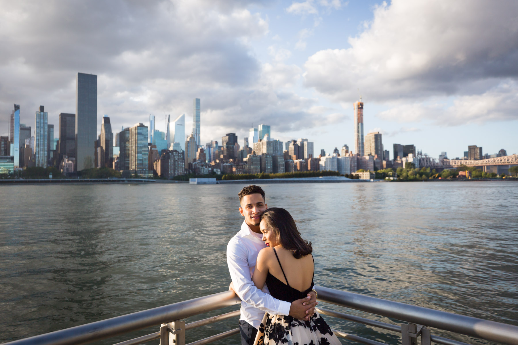 Couple hugging in front of railing with city skyline in background for an article on how to beat the summer heat during a photo shoot