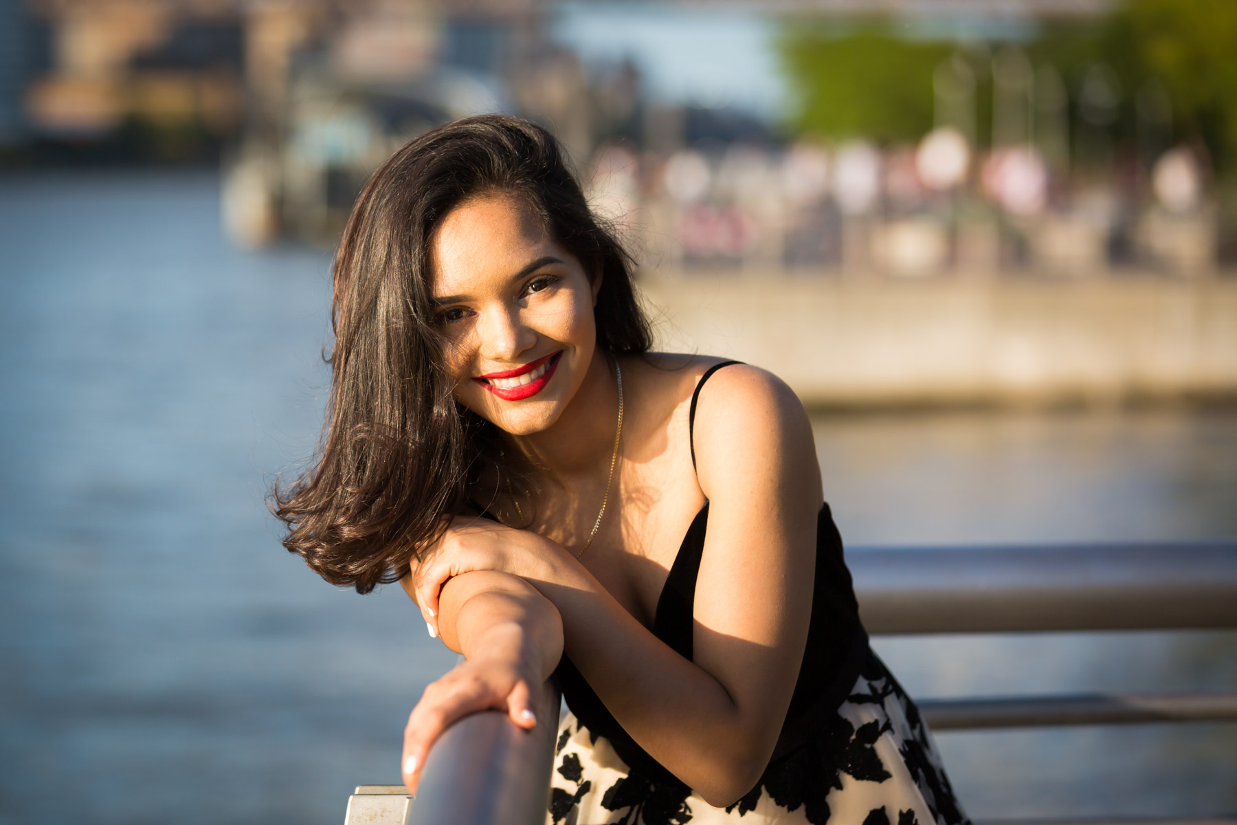 Smiling woman with brown hair and red lipstick holding onto railing for an article on how to beat the summer heat during a photo shoot