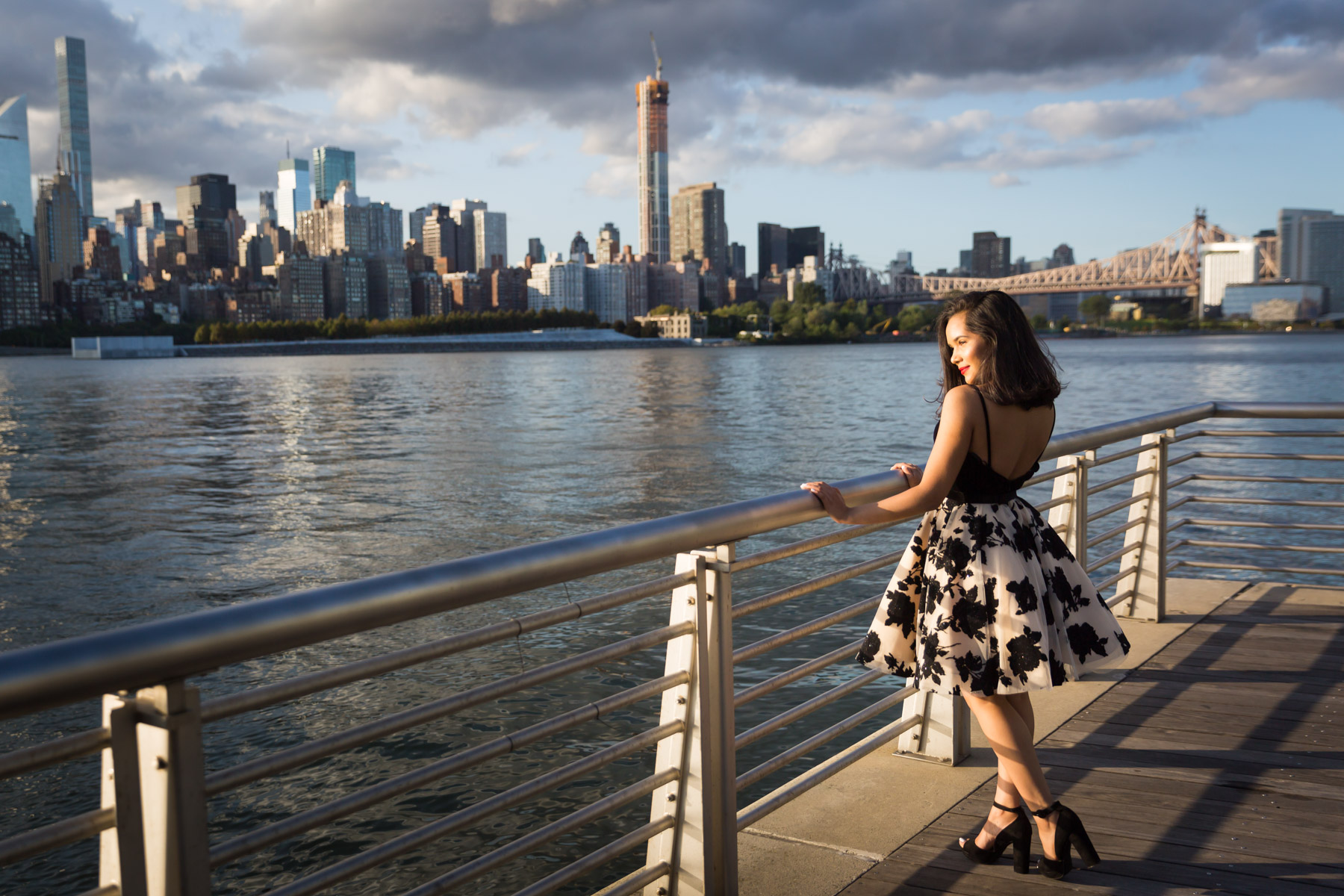 Smiling woman with brown hair and red lipstick holding onto railing for an article on how to beat the summer heat during a photo shoot