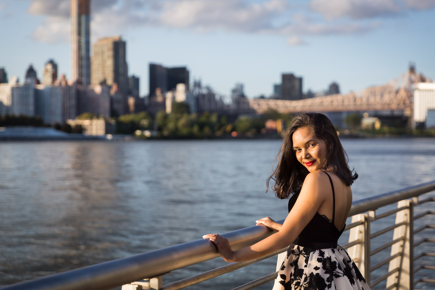 Smiling woman with brown hair and red lipstick holding onto railing for an article on how to beat the summer heat during a photo shoot