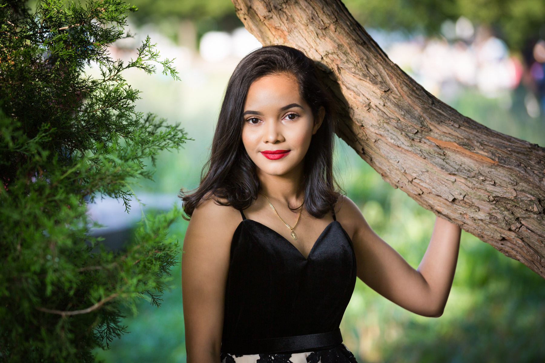 Smiling woman with brown hair and red lipstick holding onto tree for an article on how to beat the summer heat during a photo shoot