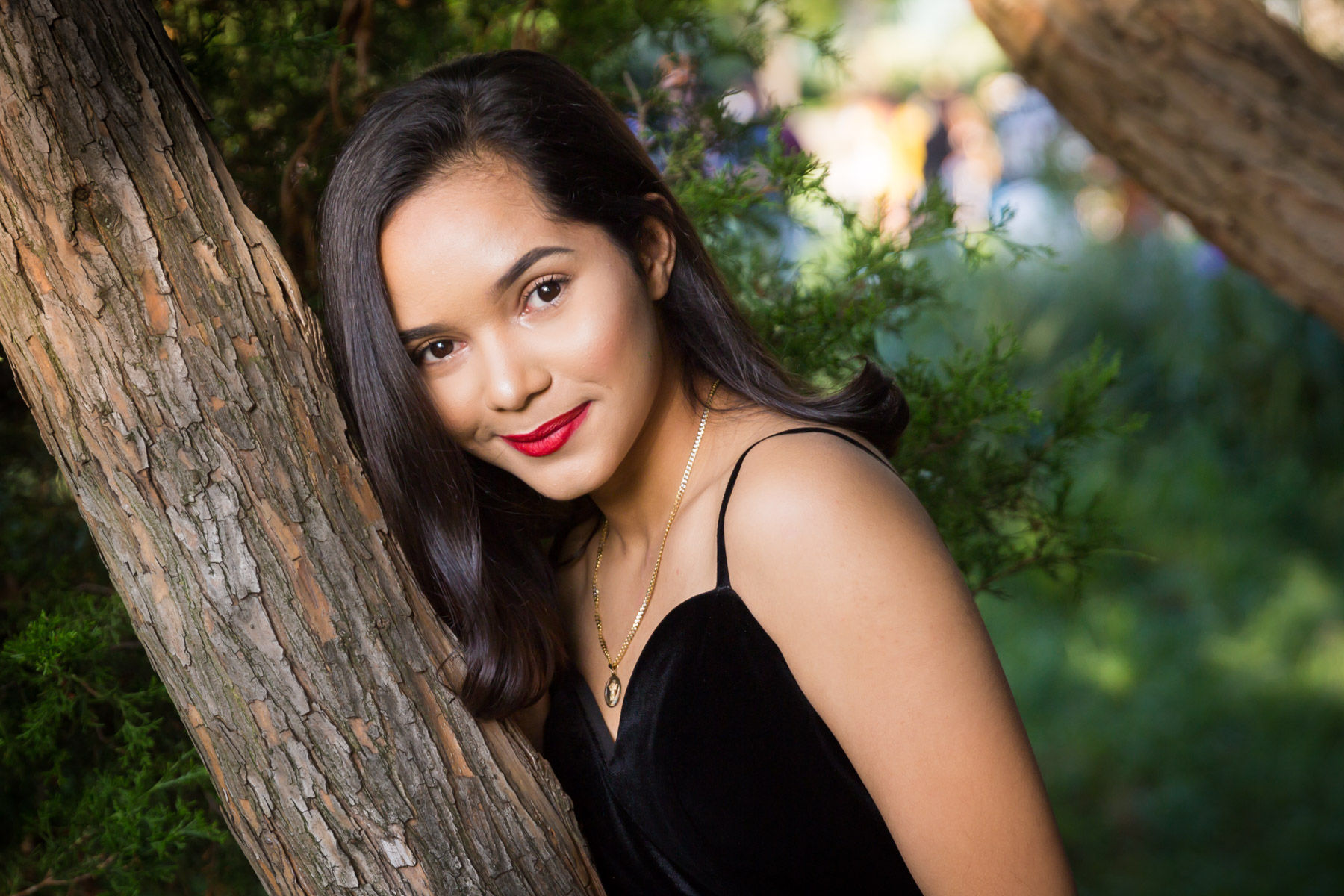 Smiling woman with brown hair and red lipstick leaning on tree for an article on how to beat the summer heat during a photo shoot