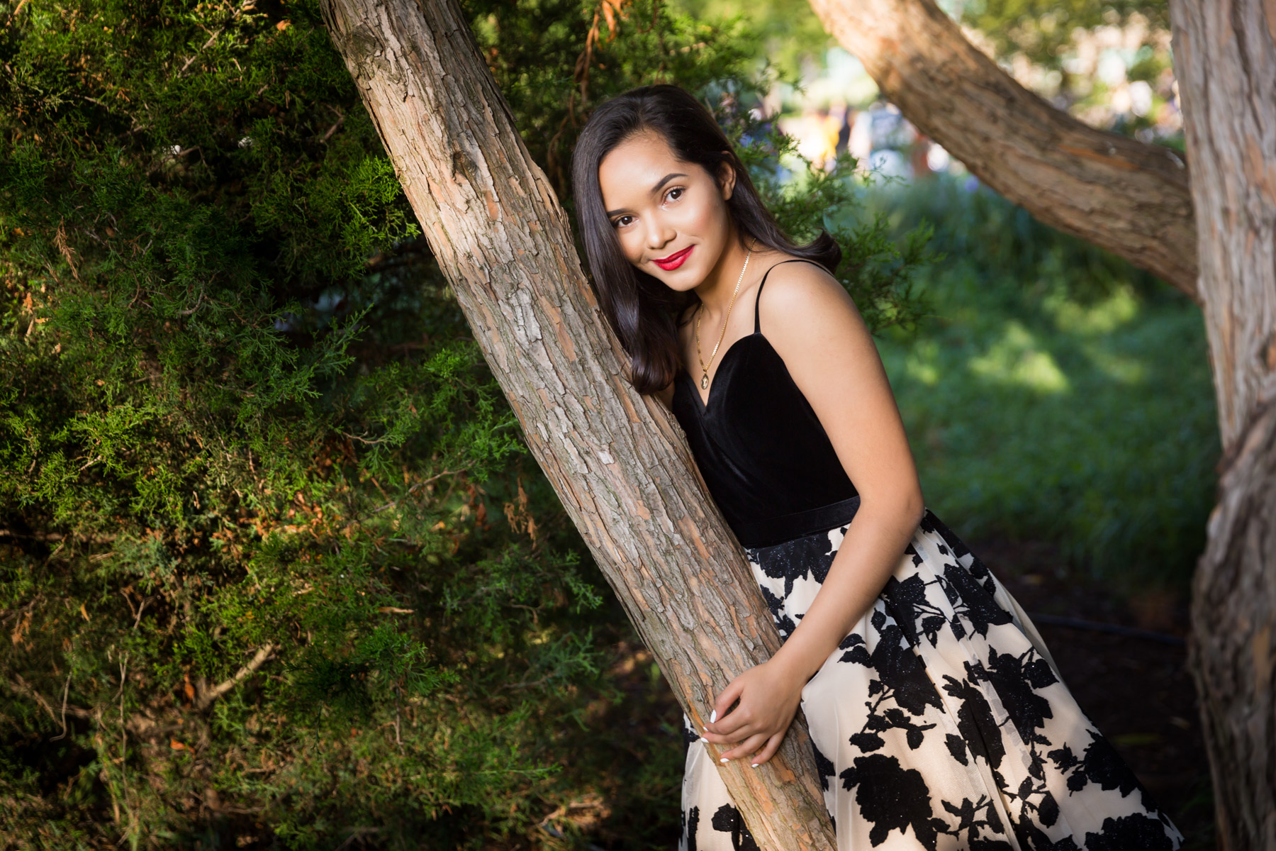 Smiling woman with brown hair and red lipstick leaning on tree for an article on how to beat the summer heat during a photo shoot