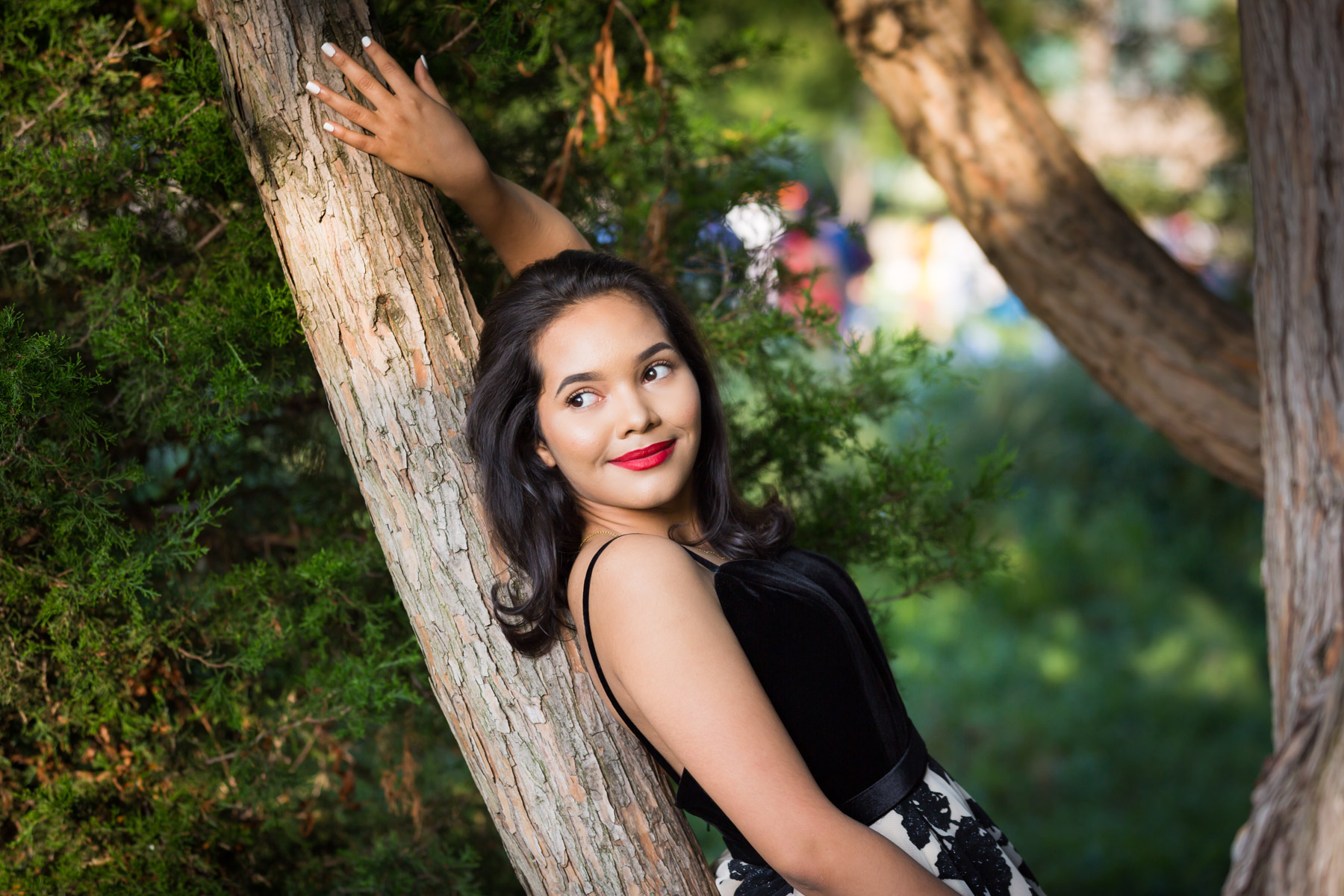 Smiling woman with brown hair and red lipstick leaning on tree for an article on how to beat the summer heat during a photo shoot