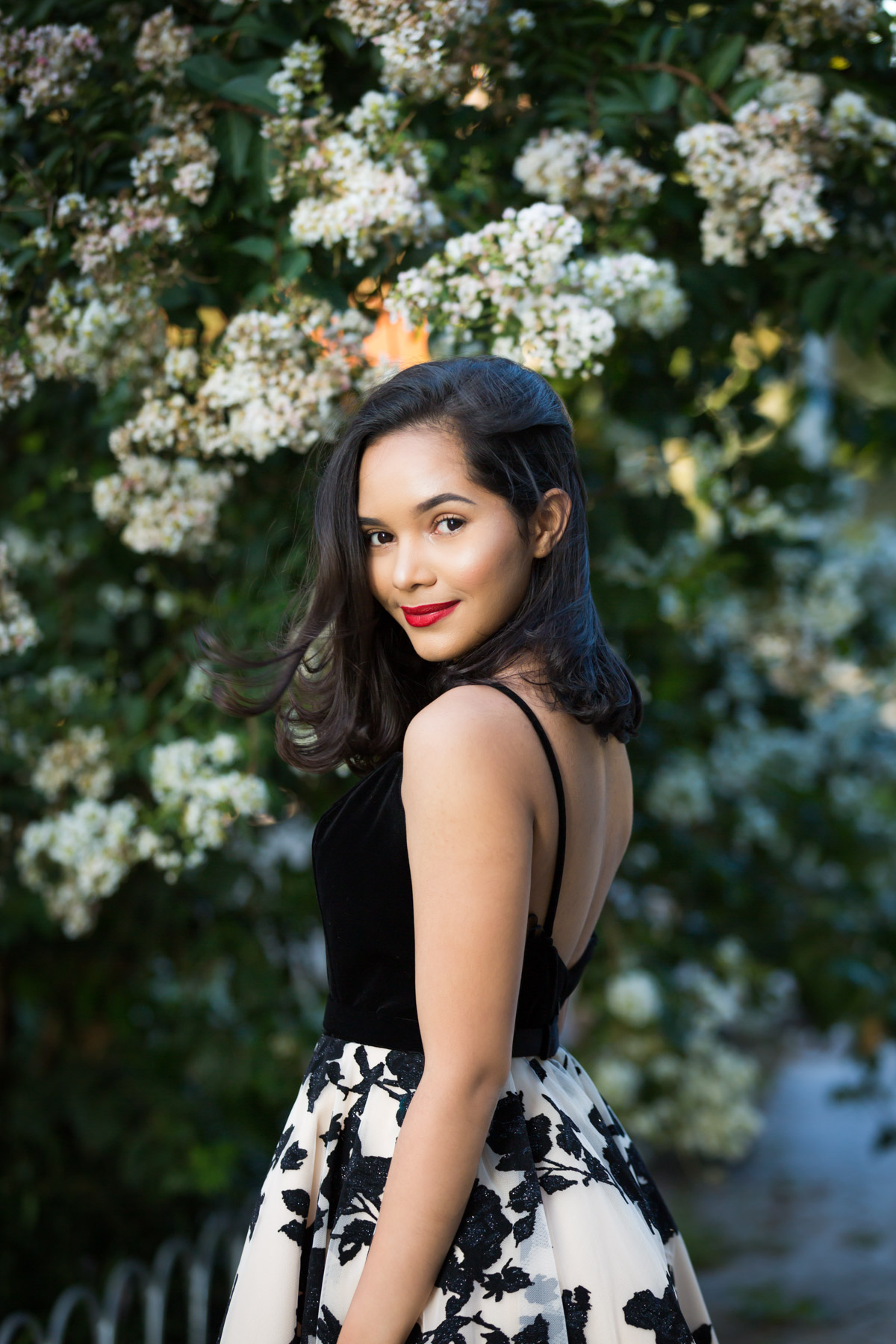 Smiling woman with brown hair and red lipstick looking over shoulder in front of bush for an article on how to beat the summer heat during a photo shoot