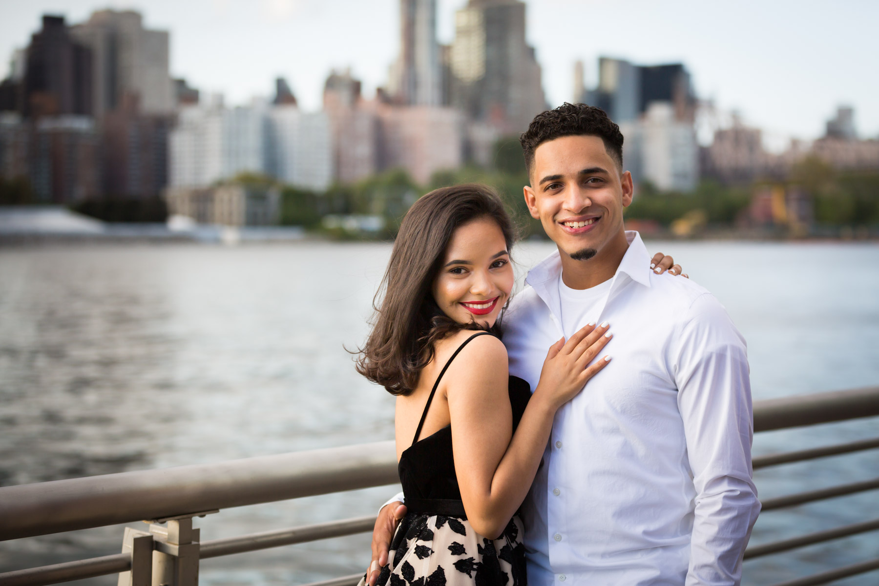 Couple hugging in front of railing with city skyline in background for an article on how to beat the summer heat during a photo shoot